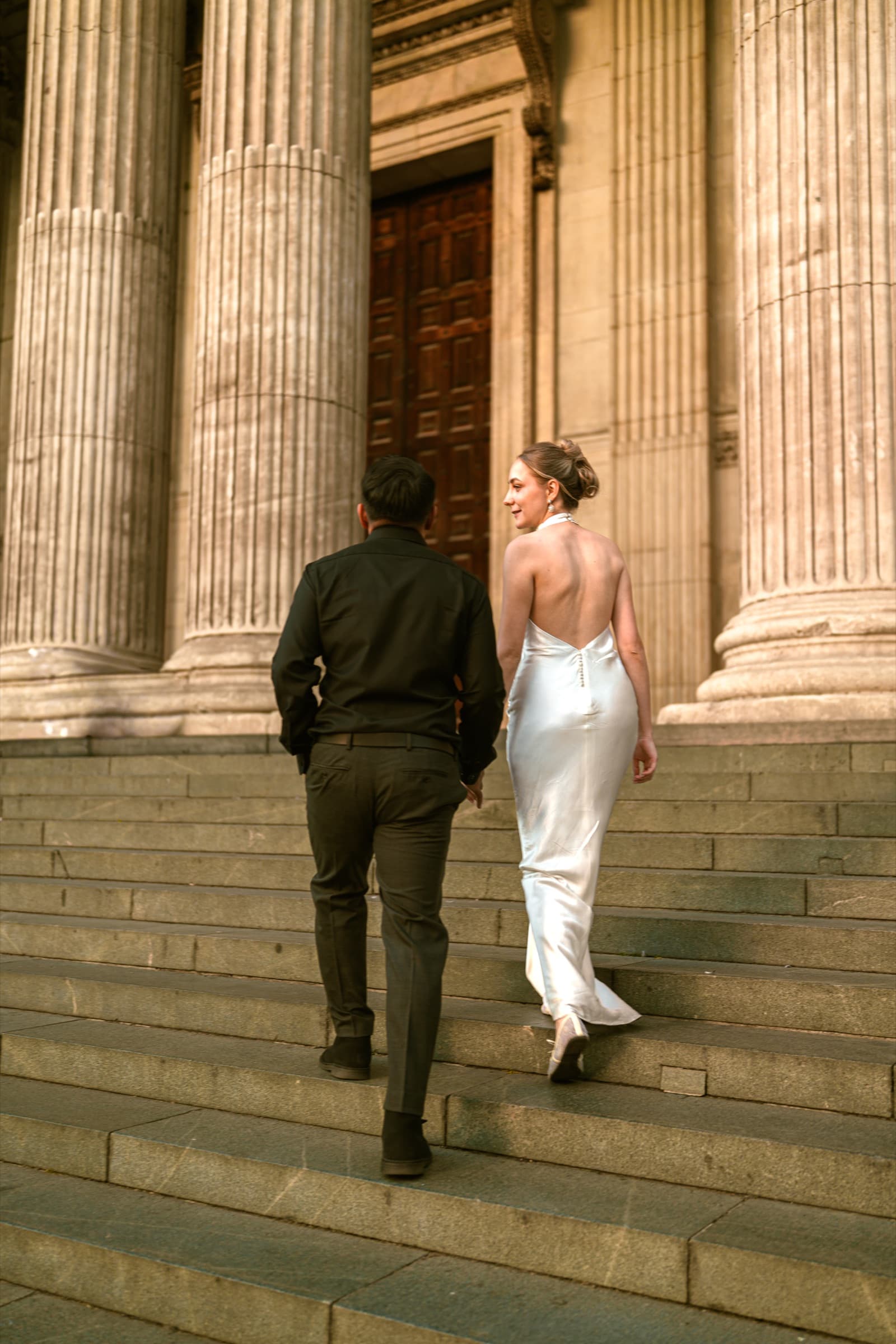 A couple climbing the steps of St Paul’s Cathedral towards the west doors, columns rising either side