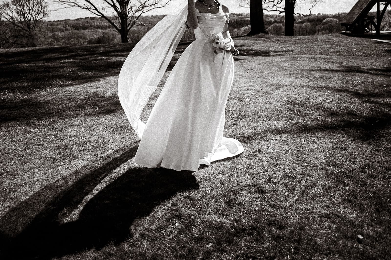 Black and white photograph of the bride’s veil catching the light on the lawn