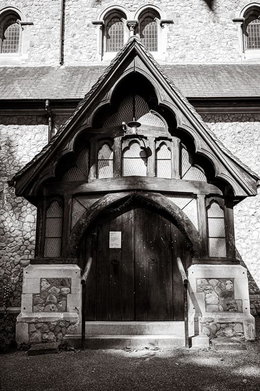 The timber Gothic porch and arched oak door of St John’s Church, East Dulwich, in black and white