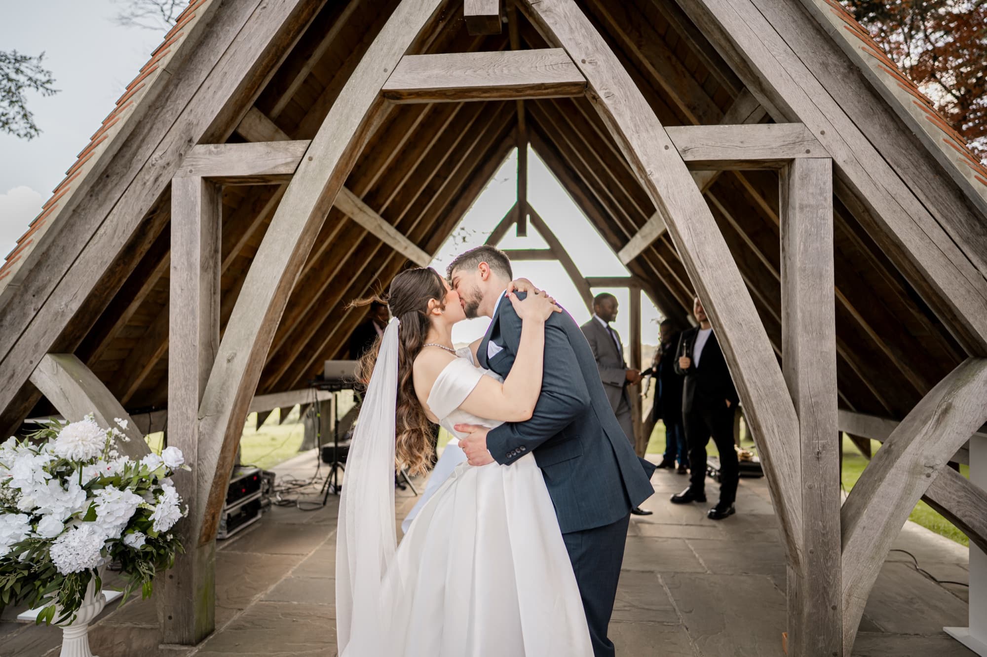 Bride and groom share their first kiss framed symmetrically inside the oak A-frame glass pavilion at Highley Manor