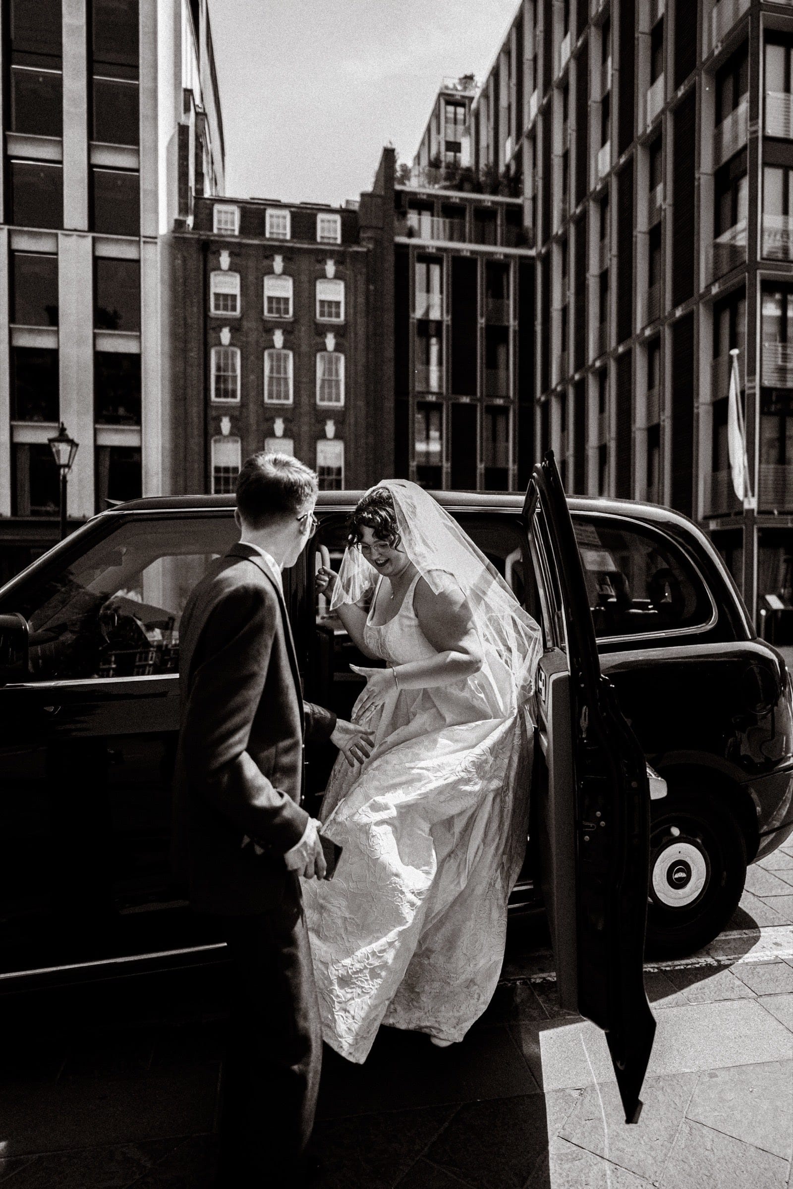 A bride stepping out of a black cab on a London street on her wedding morning