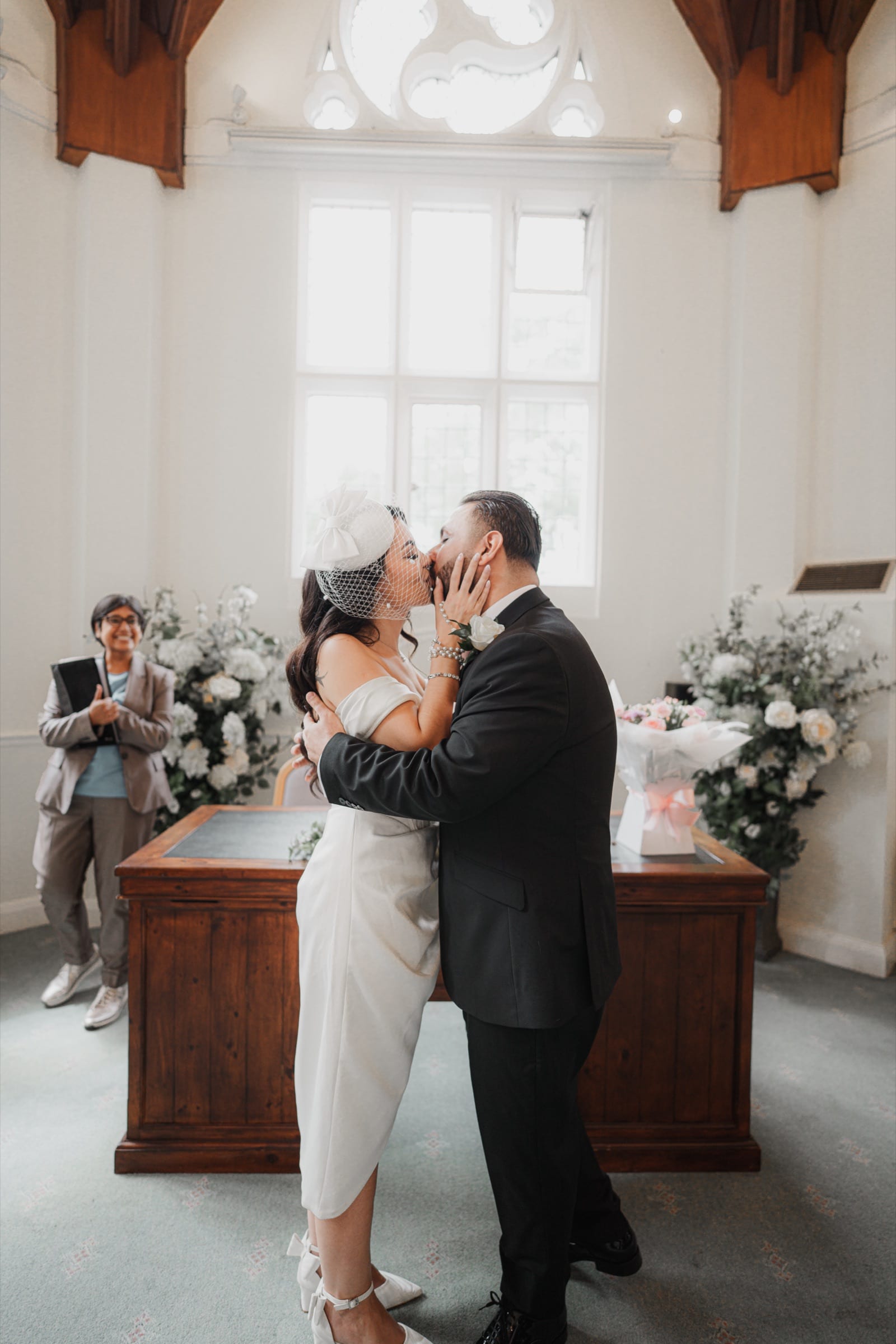 A couple’s first kiss as the registrar looks on at a London register office wedding