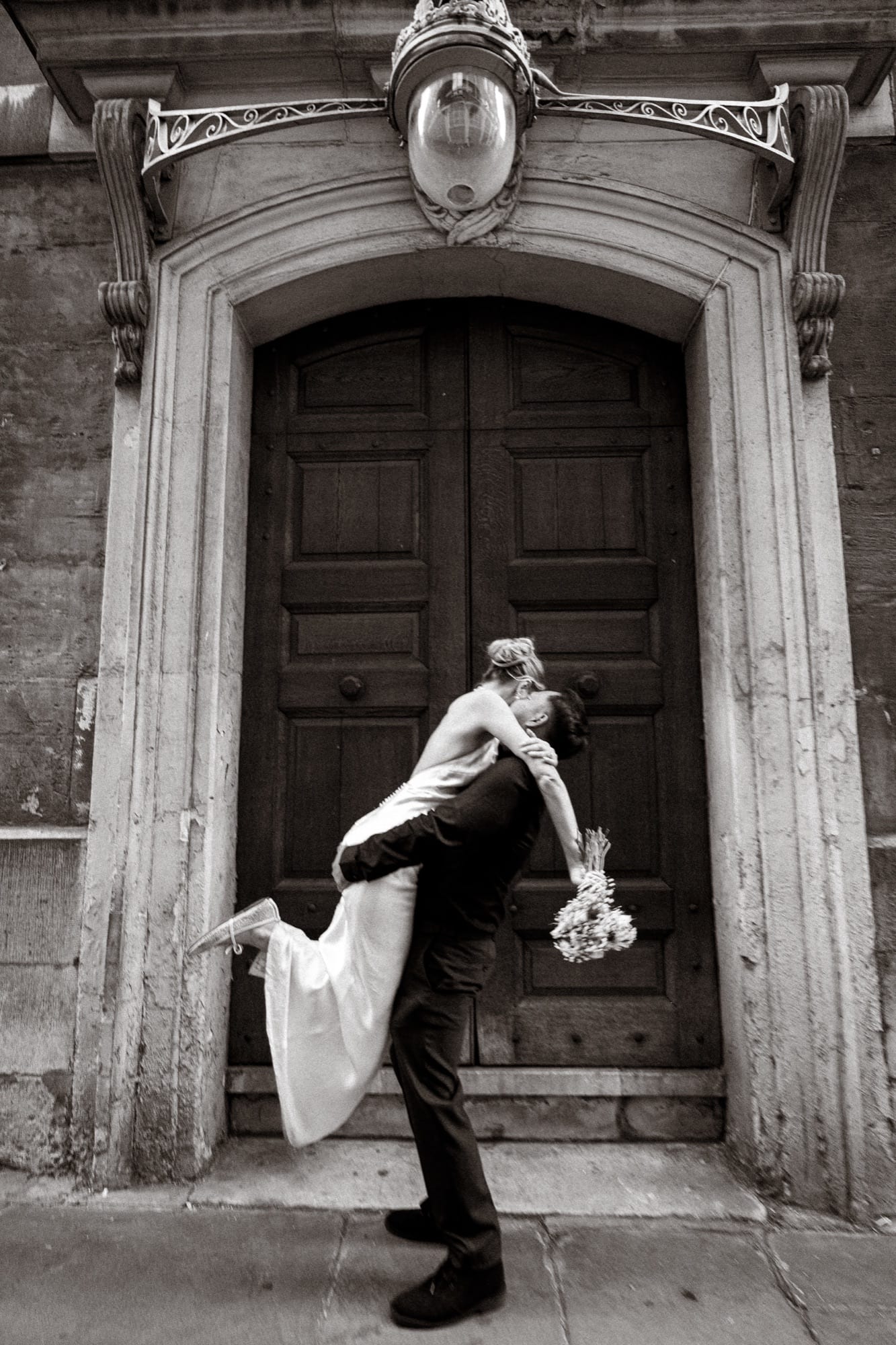 A groom lifting his bride off her feet in a stone doorway near St Paul’s, in black and white