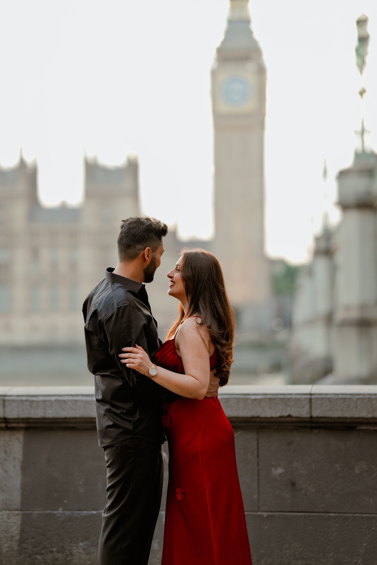 A couple in evening outfits embracing at the river wall with Big Ben soft in the background