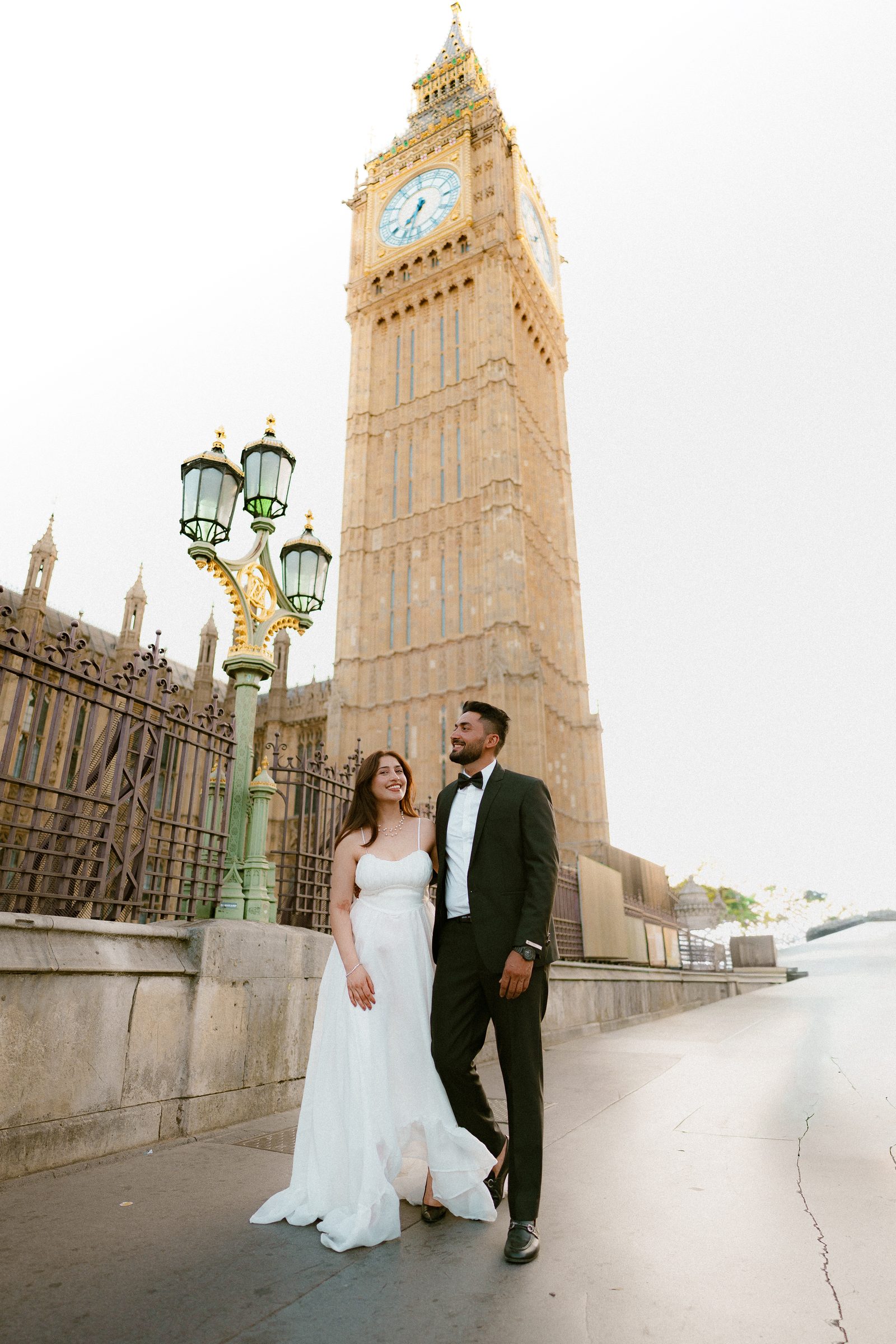 A couple standing beneath an ornate black lamp post at the end of Westminster Bridge with Big Ben rising behind them