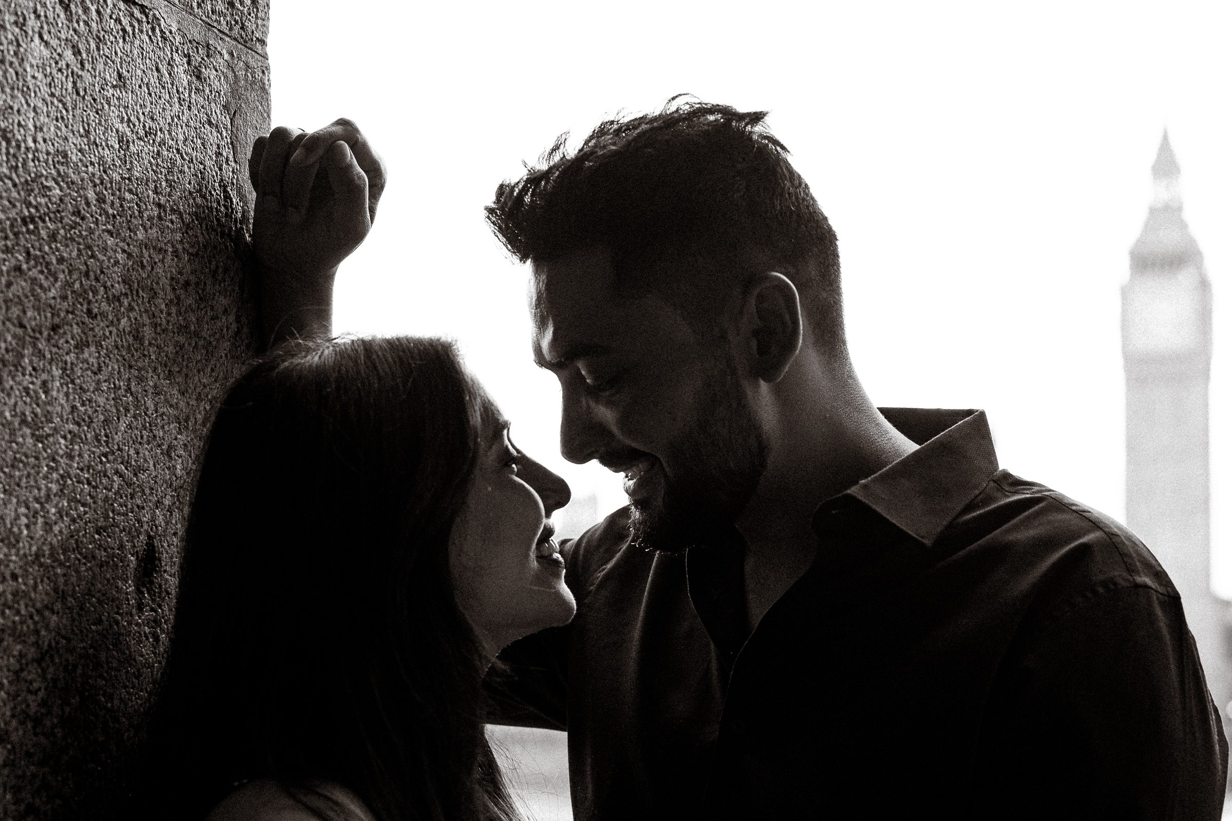 A close black and white frame of a couple almost kissing, deep shadow and soft window of sky behind them