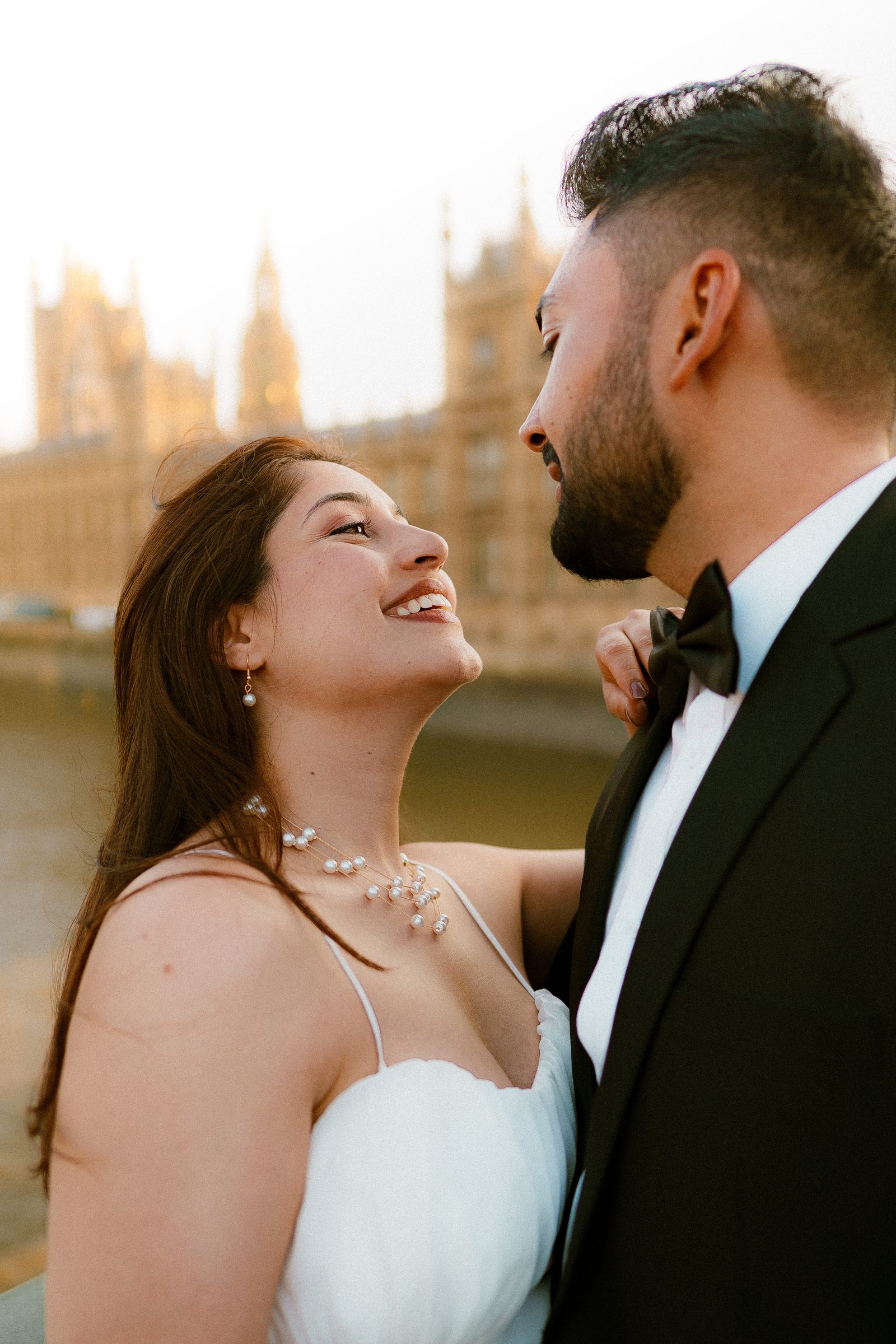 Prachi laughing up at Rohit on Westminster Bridge, the Houses of Parliament soft behind them in golden light