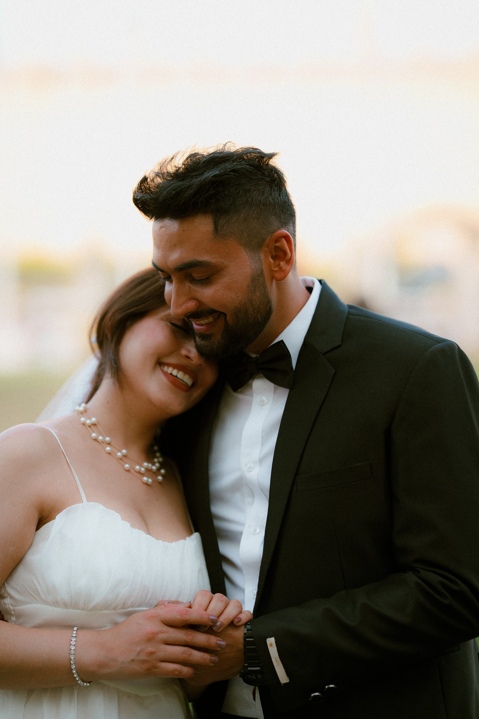 Prachi tucked under Rohit’s chin, laughing, in a white gown and black suit on a Westminster evening