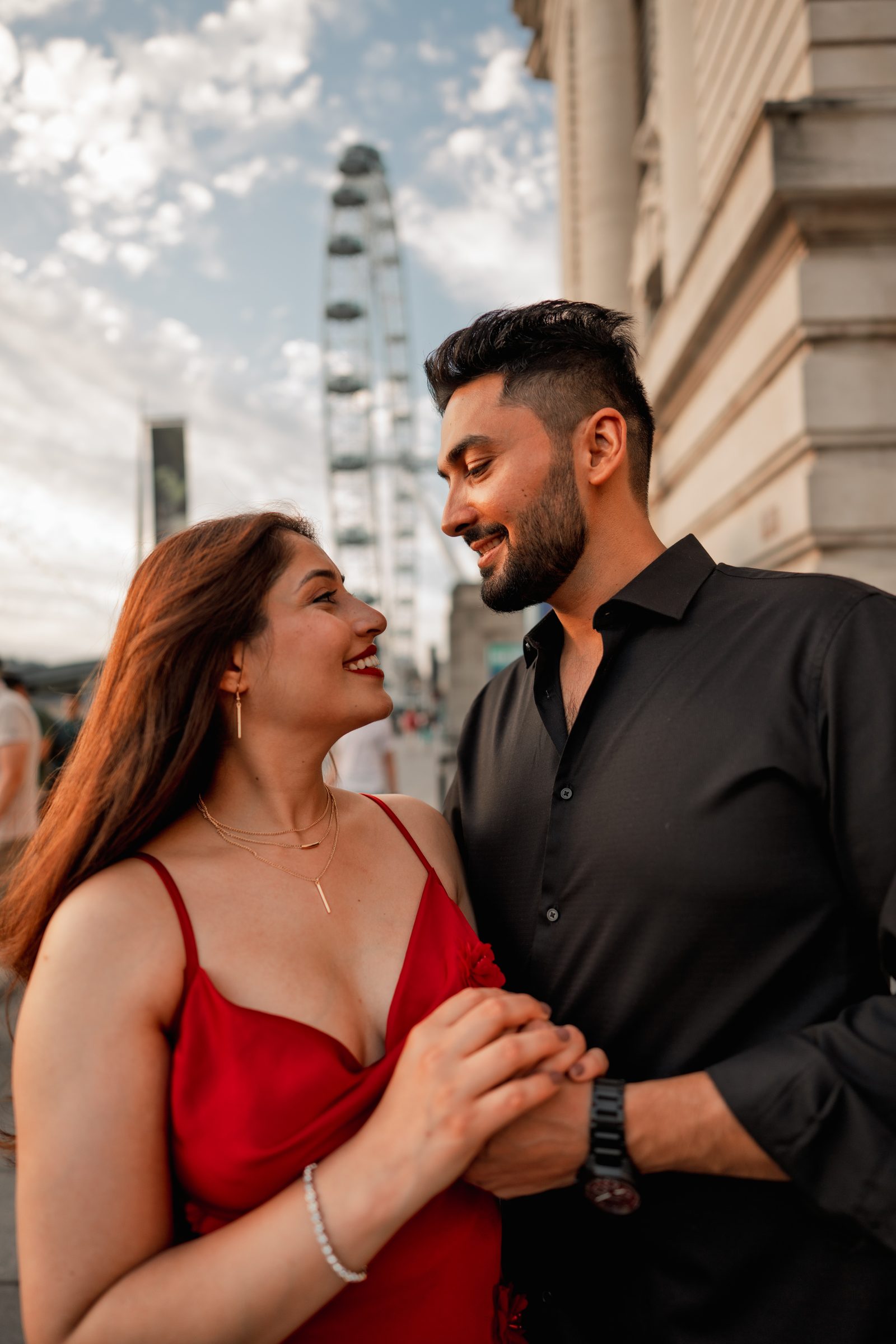 Prachi in a red silk dress laughing with Rohit outside County Hall on the South Bank, the London Eye above them