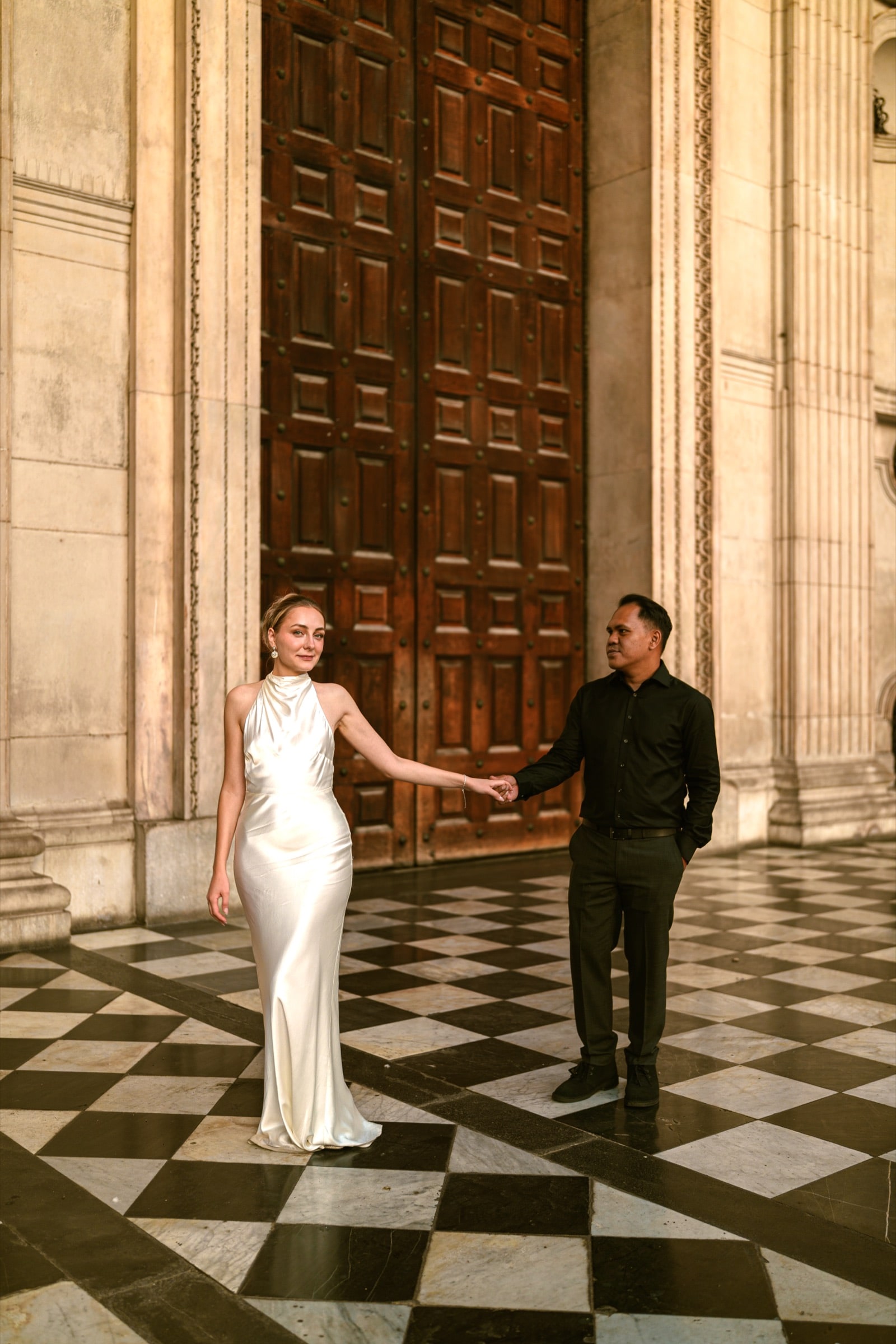 A couple hand in hand on the chequerboard floor before the great west doors of St Paul's Cathedral