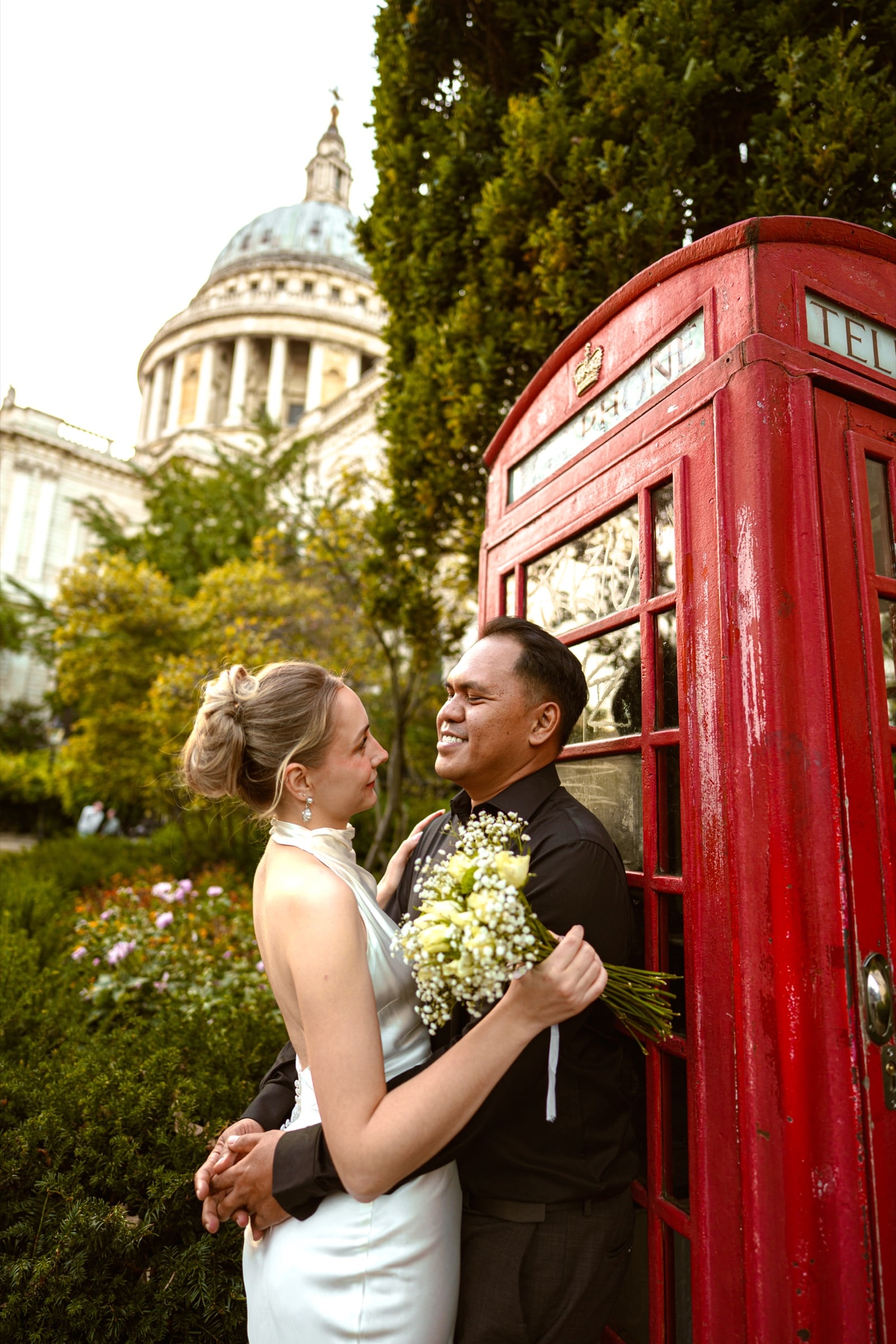 A couple laughing beside a red telephone box with the dome of St Paul's Cathedral behind them