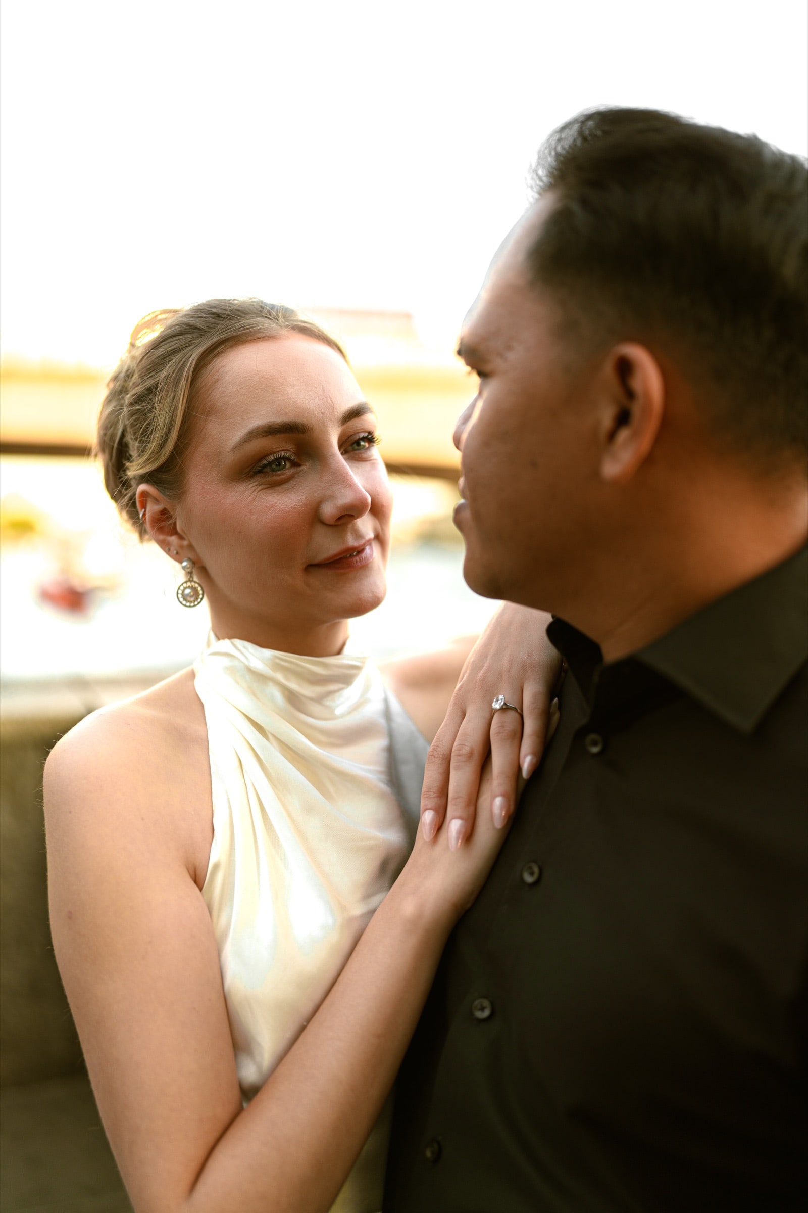 A close riverside portrait of a couple at golden hour by the Thames, her engagement ring catching the light