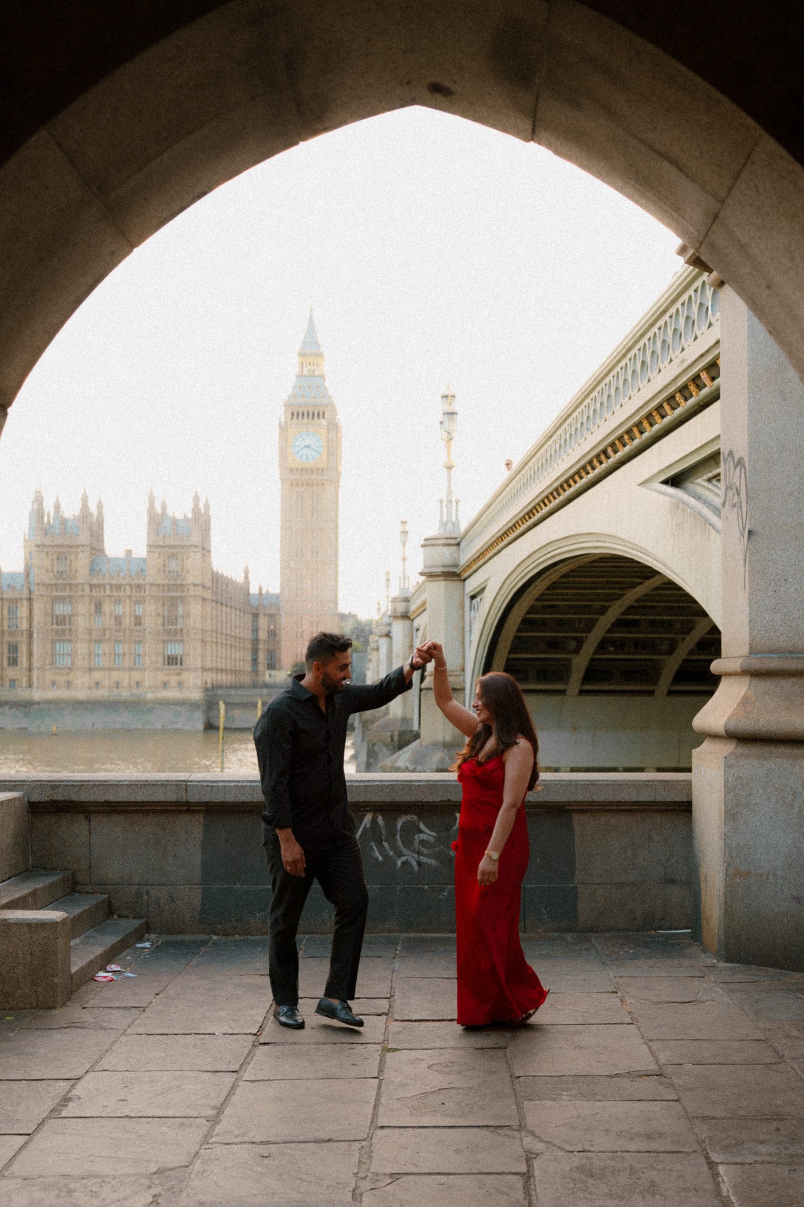 A couple dancing beneath a stone arch on the South Bank, Big Ben and Westminster Bridge framed in the opening behind them