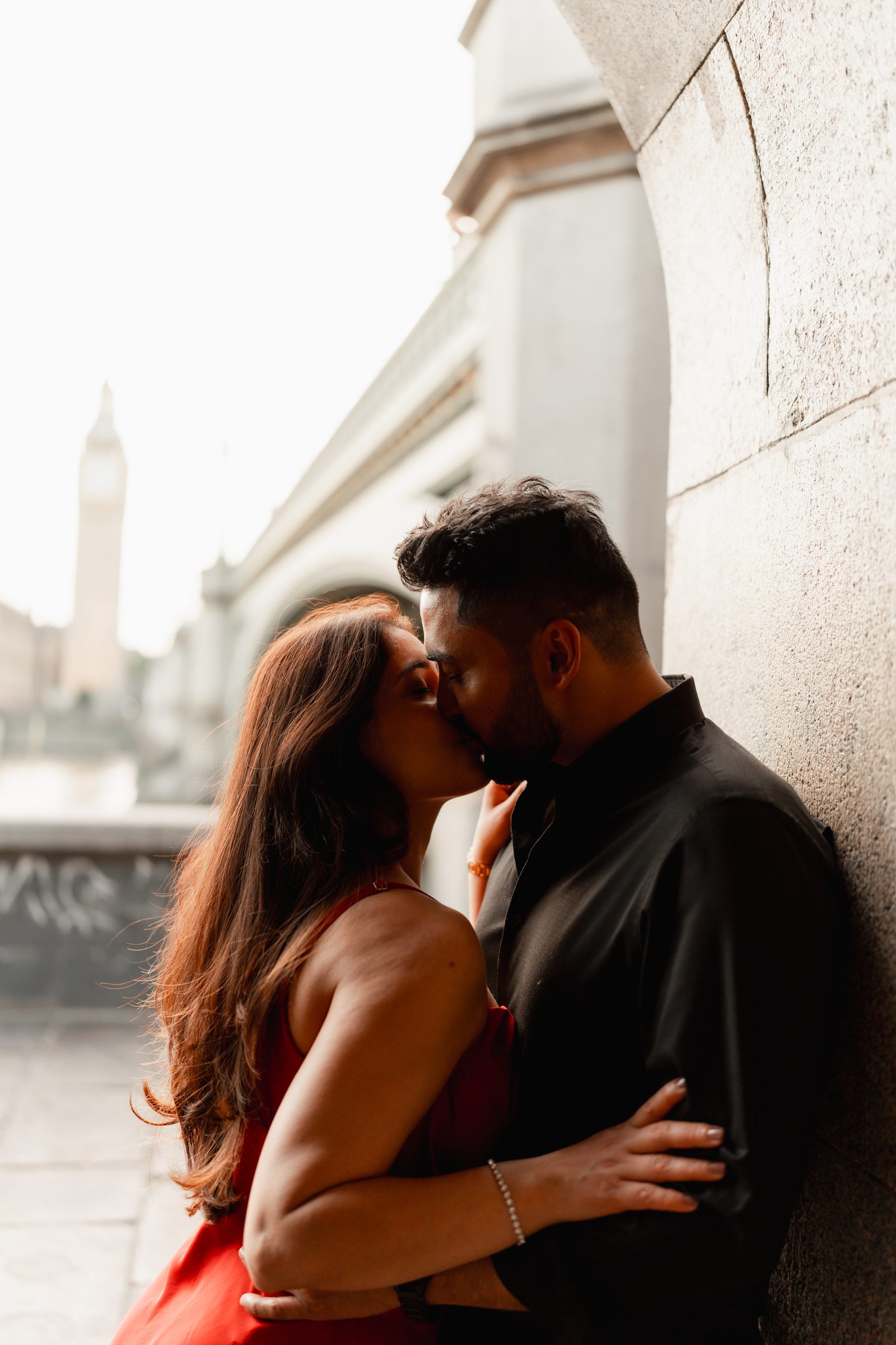 A couple kissing against warm stone under an arch on the South Bank during a London pre-wedding shoot