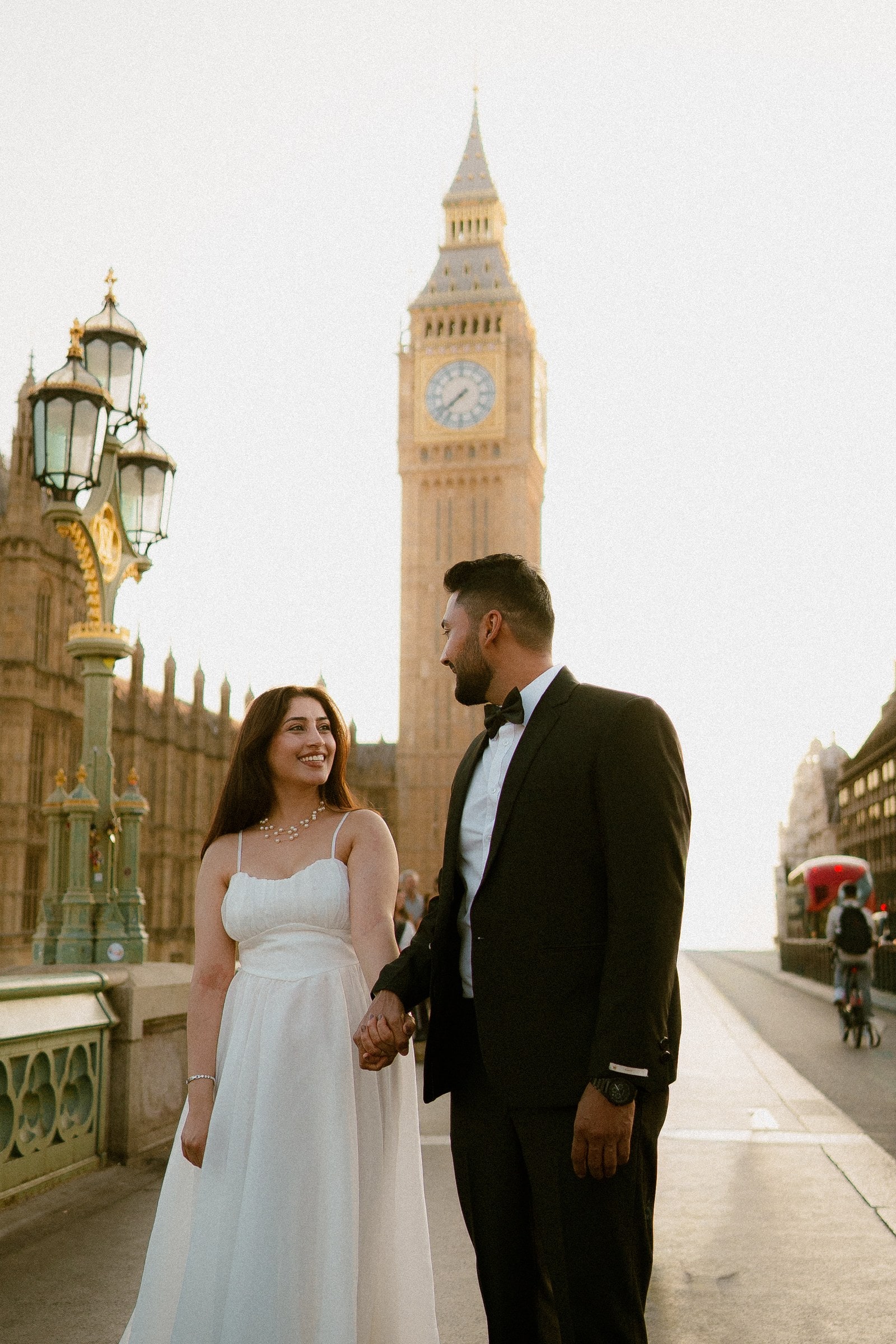 A couple holding hands beside the ornate green lamp posts on Westminster Bridge, Big Ben glowing gold behind