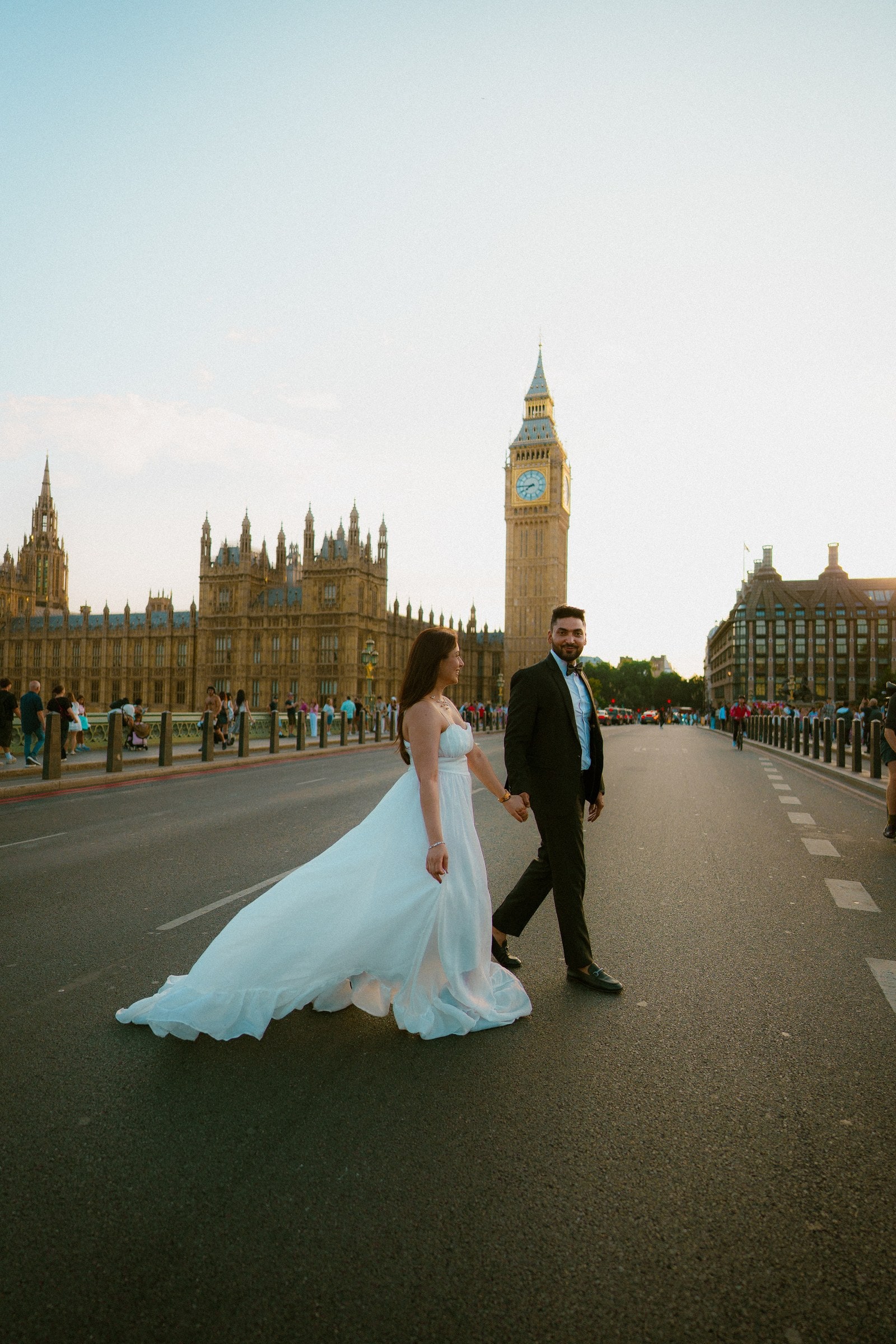 A couple crossing the road on Westminster Bridge, the train of a white wedding dress sweeping across the tarmac towards Big Ben