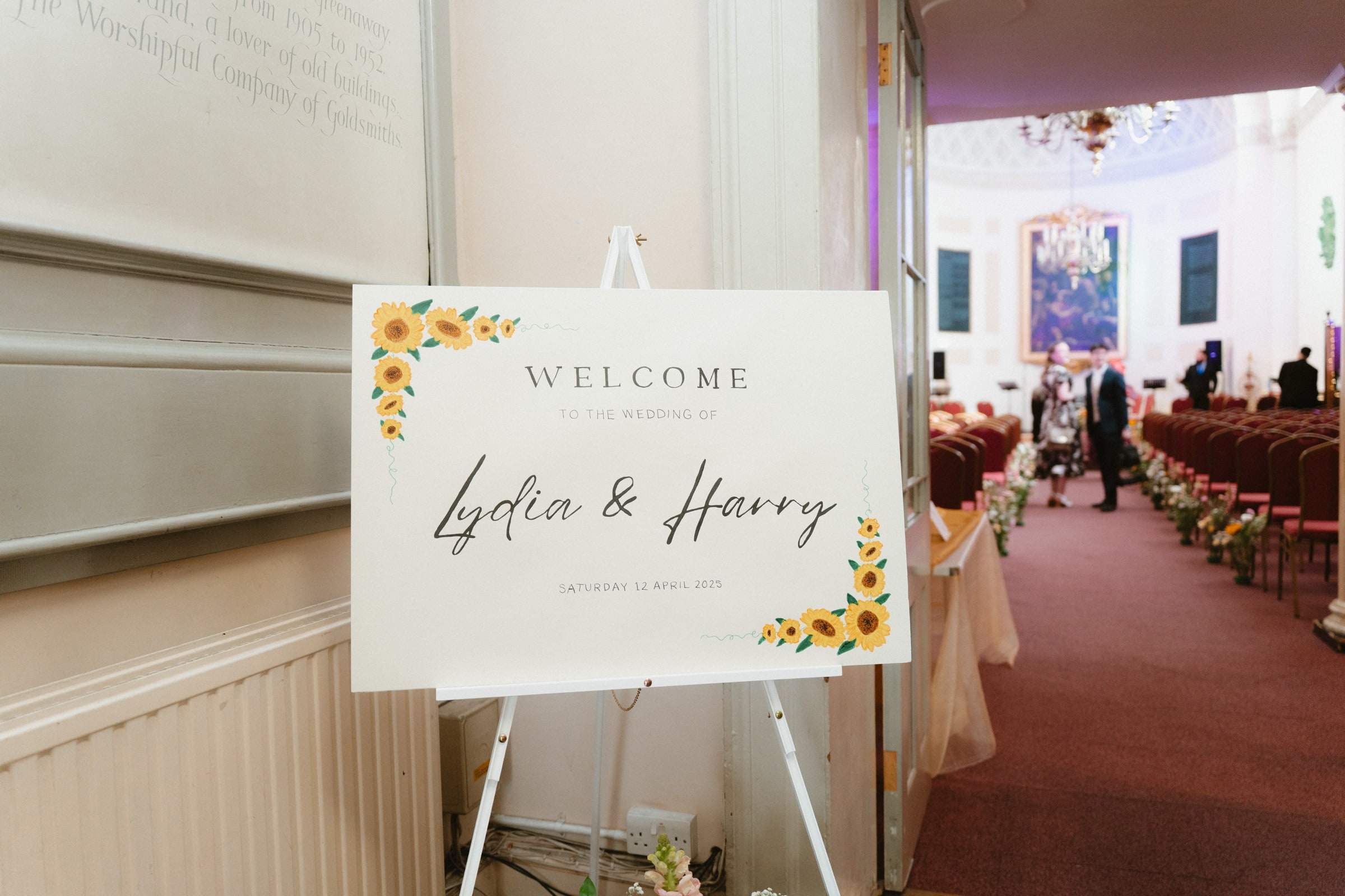 Welcome sign in the aisle of All Hallows-on-the-Wall, the red-chaired nave and chandelier behind, City of London