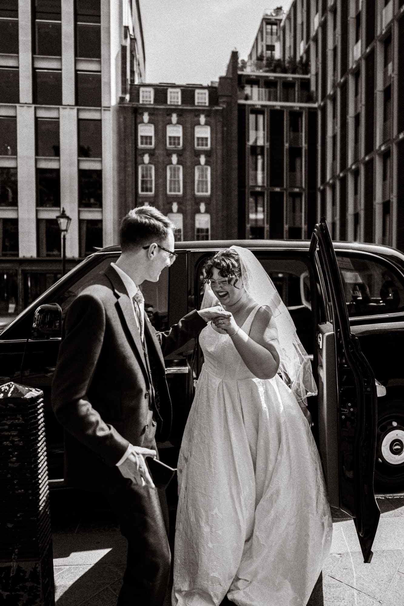 Black and white photograph of the bride stepping from a classic black London cab in the West End