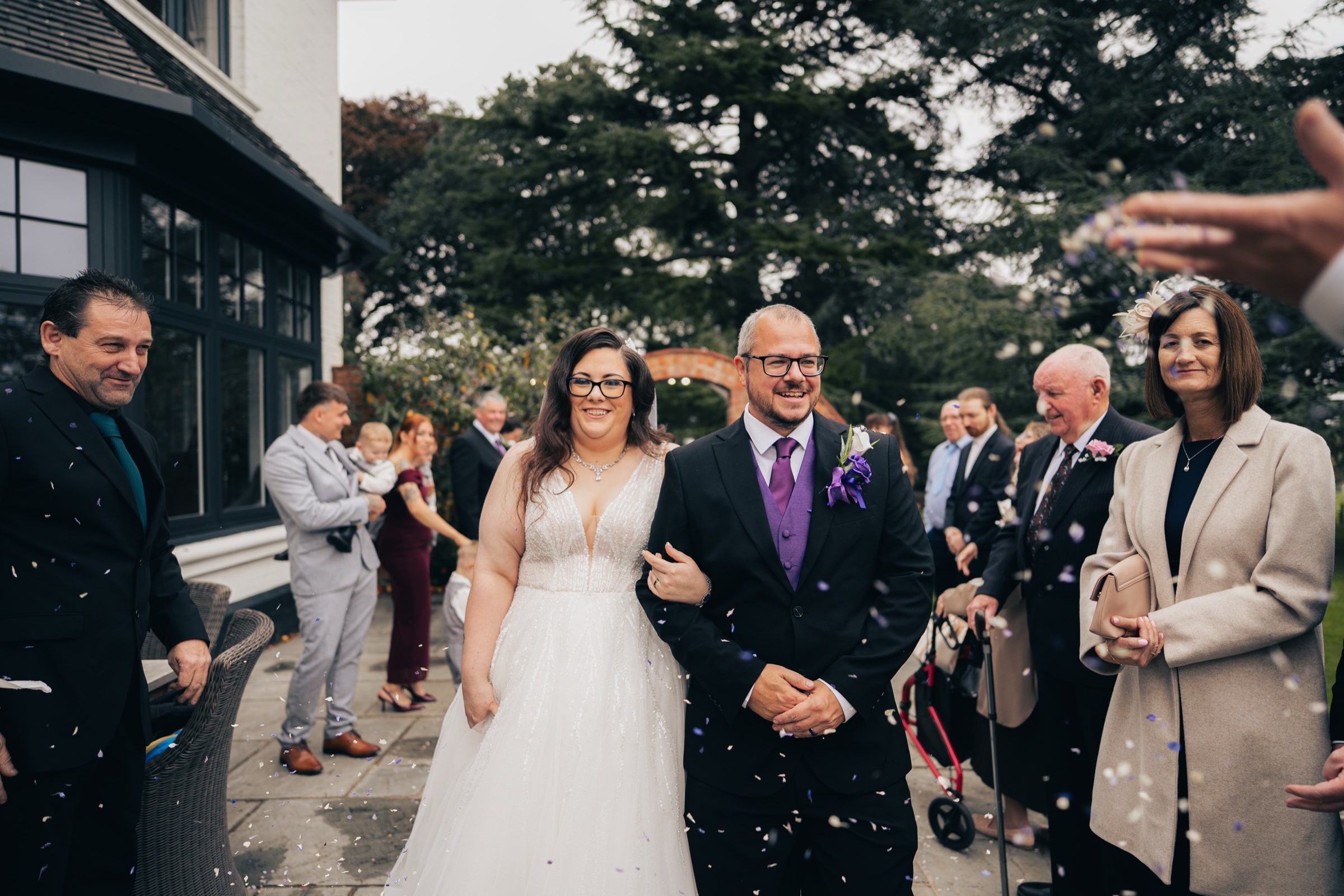 Newlyweds walking through a shower of confetti thrown by guests at Ashton Lodge Country House