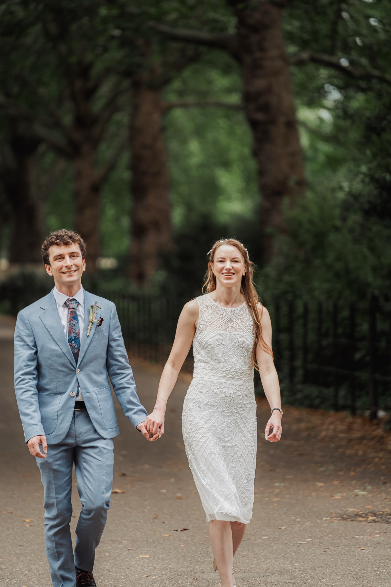 A couple walking a tree-lined avenue in a South West London park after their wedding
