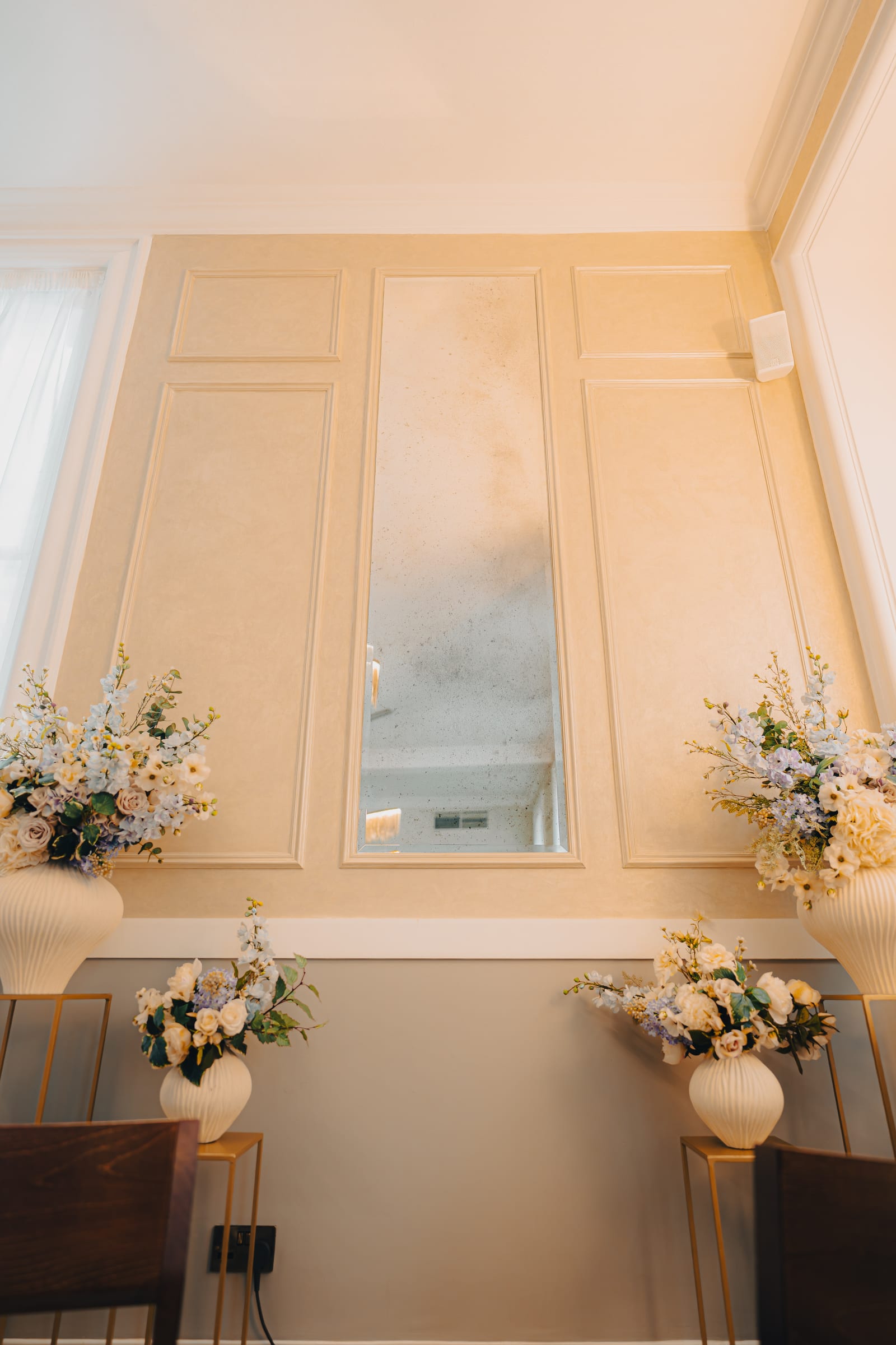 Floral arrangements either side of a tall window in a ceremony room at Chelsea Old Town Hall