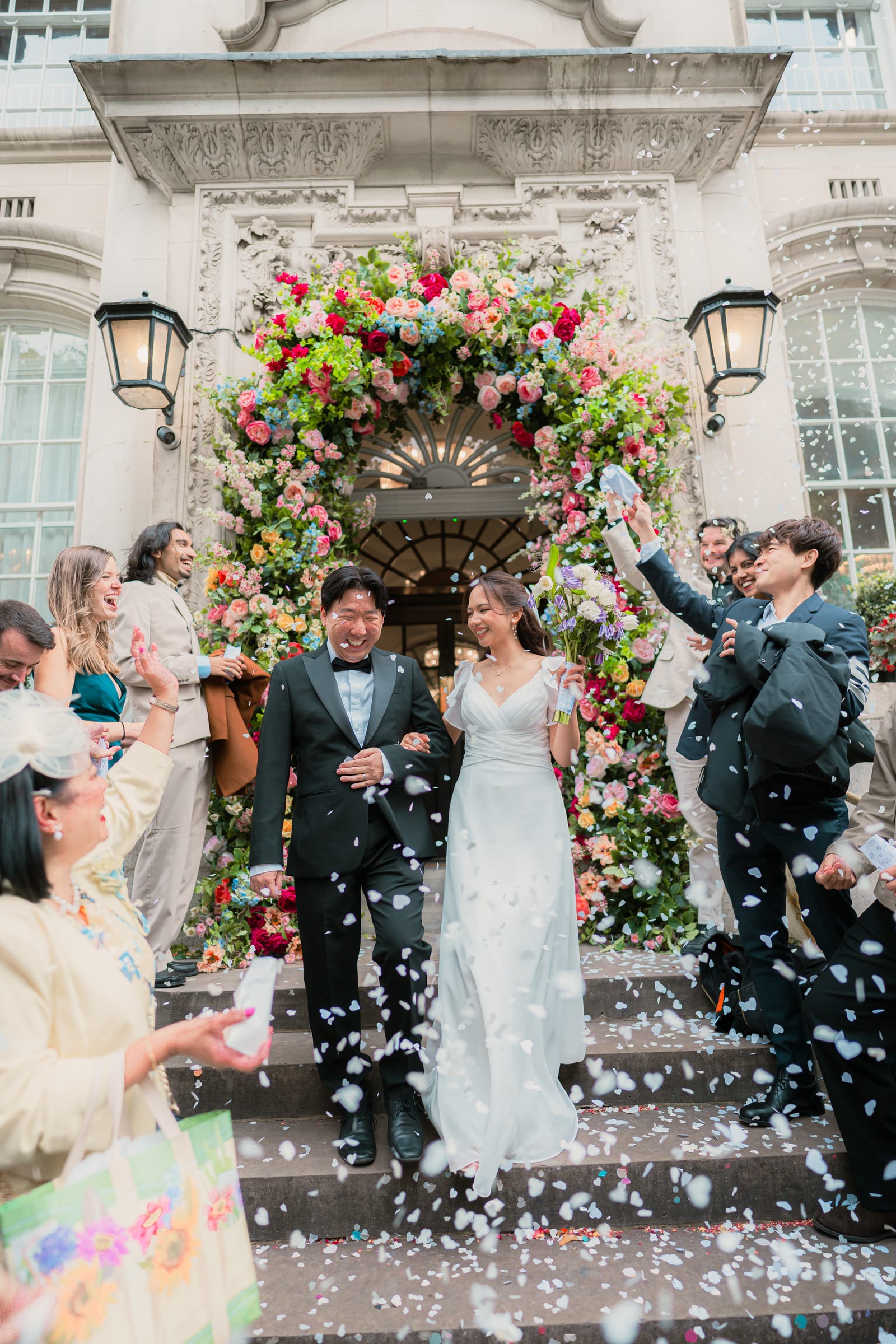 Bride and groom walking down the front steps of Chelsea Old Town Hall through a shower of petal confetti, guests lining the steps