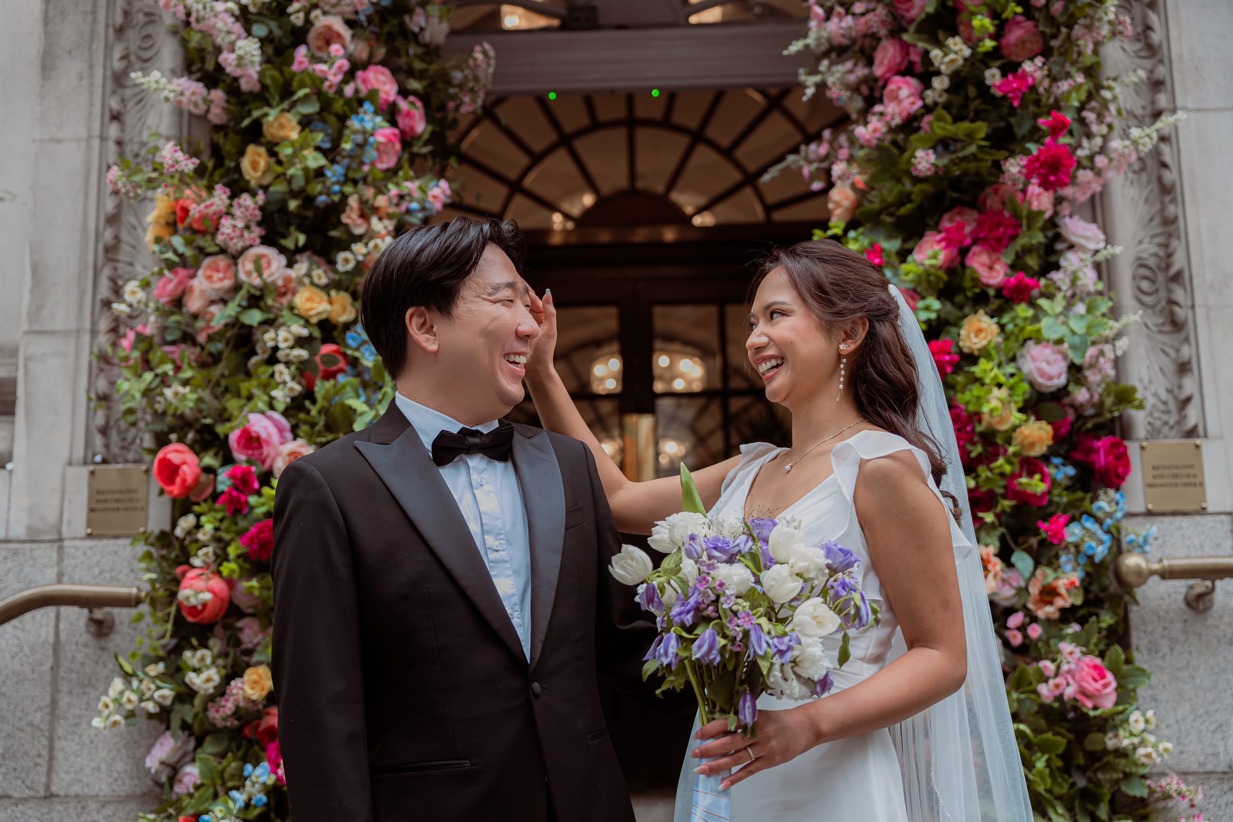 Bride and groom embracing beneath the floral-arched King’s Road entrance of Chelsea Old Town Hall