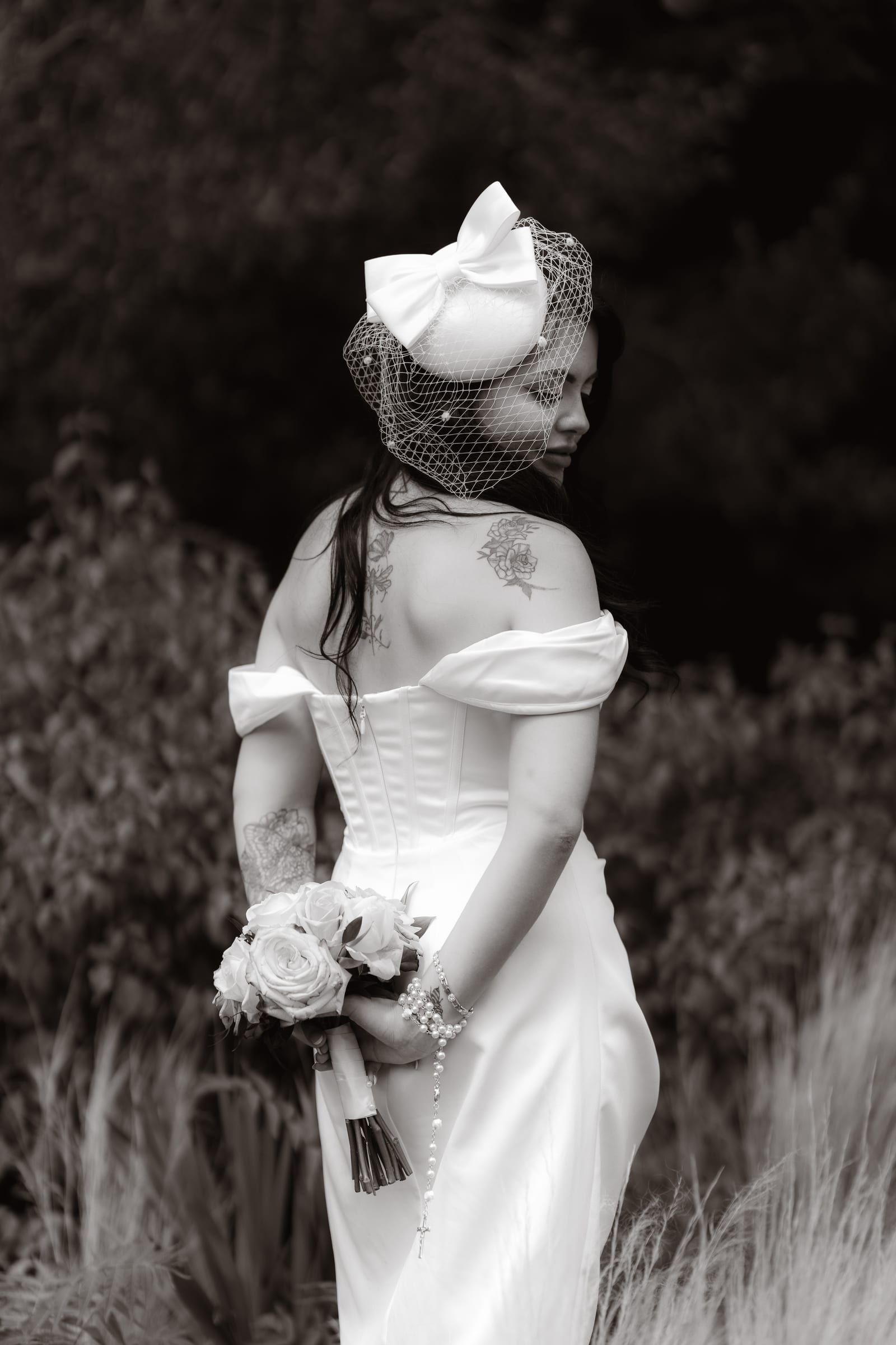 The back of a bride’s bow and birdcage veil among tall grasses at Cheshunt Register Office, in black and white