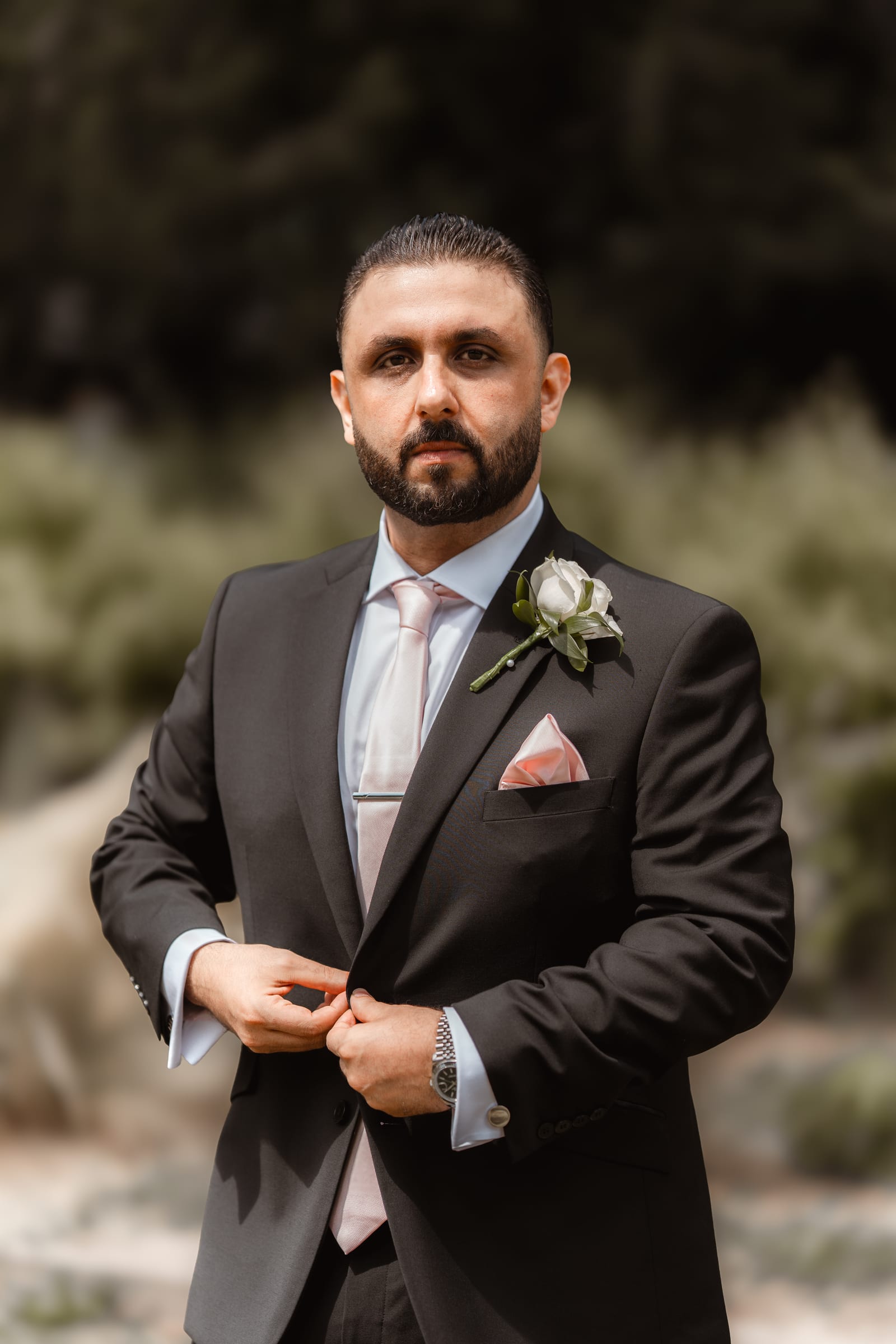 A groom buttoning his jacket for a portrait among the greenery in the grounds of Cheshunt Register Office