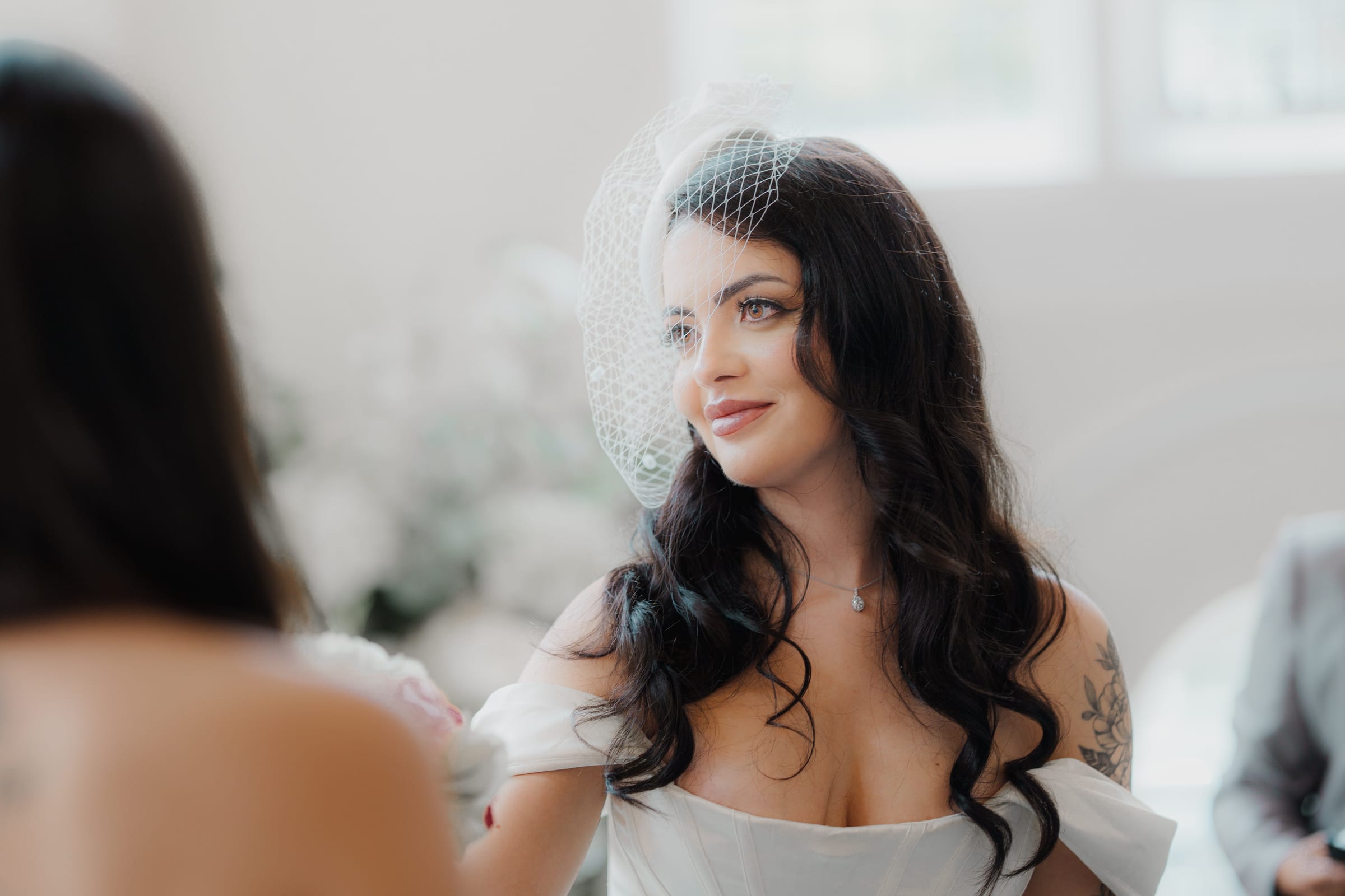 A bride in a birdcage veil lit by soft window light during her register office ceremony