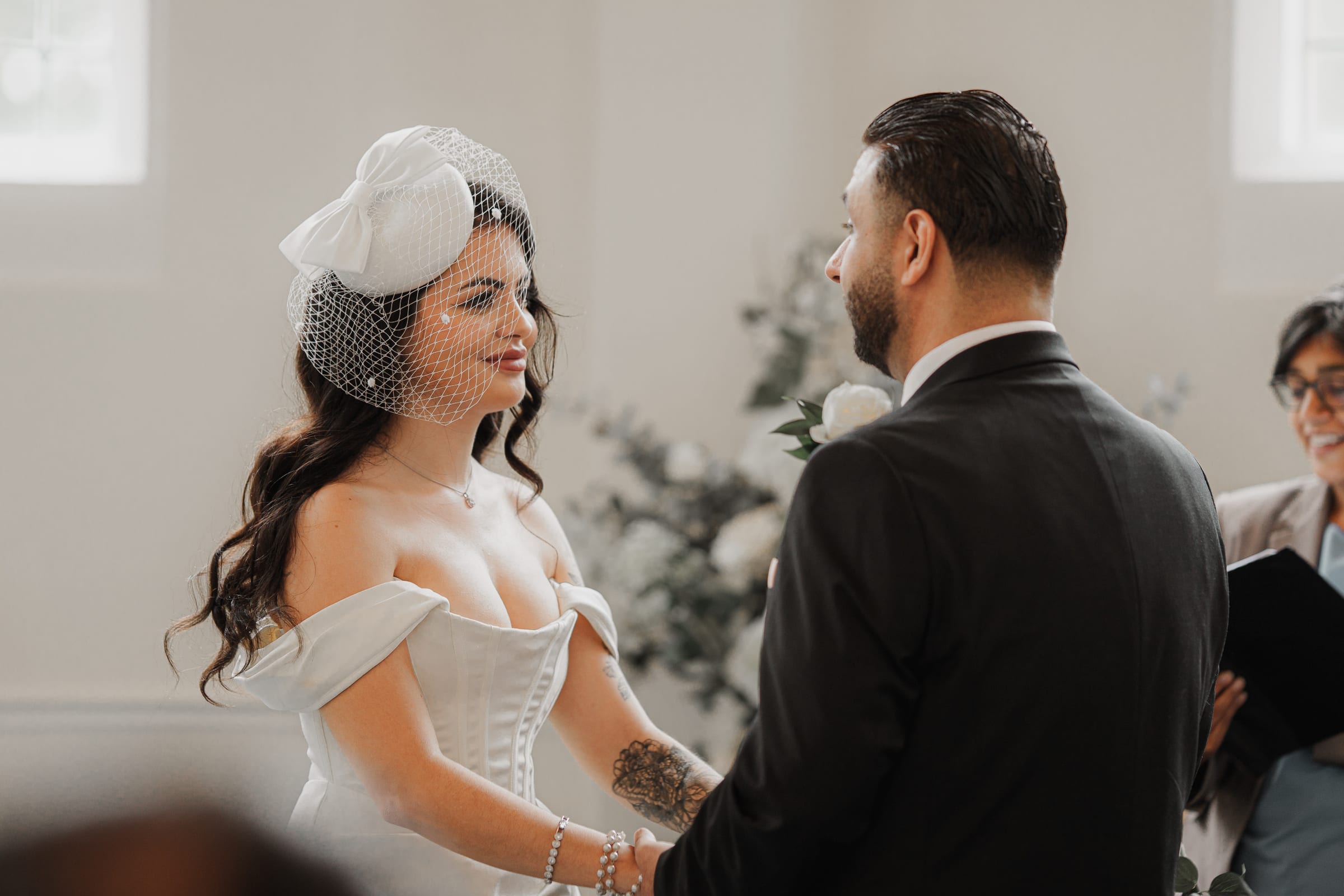 A bride in a birdcage veil facing her groom as the registrar leads the ceremony at Cheshunt Register Office
