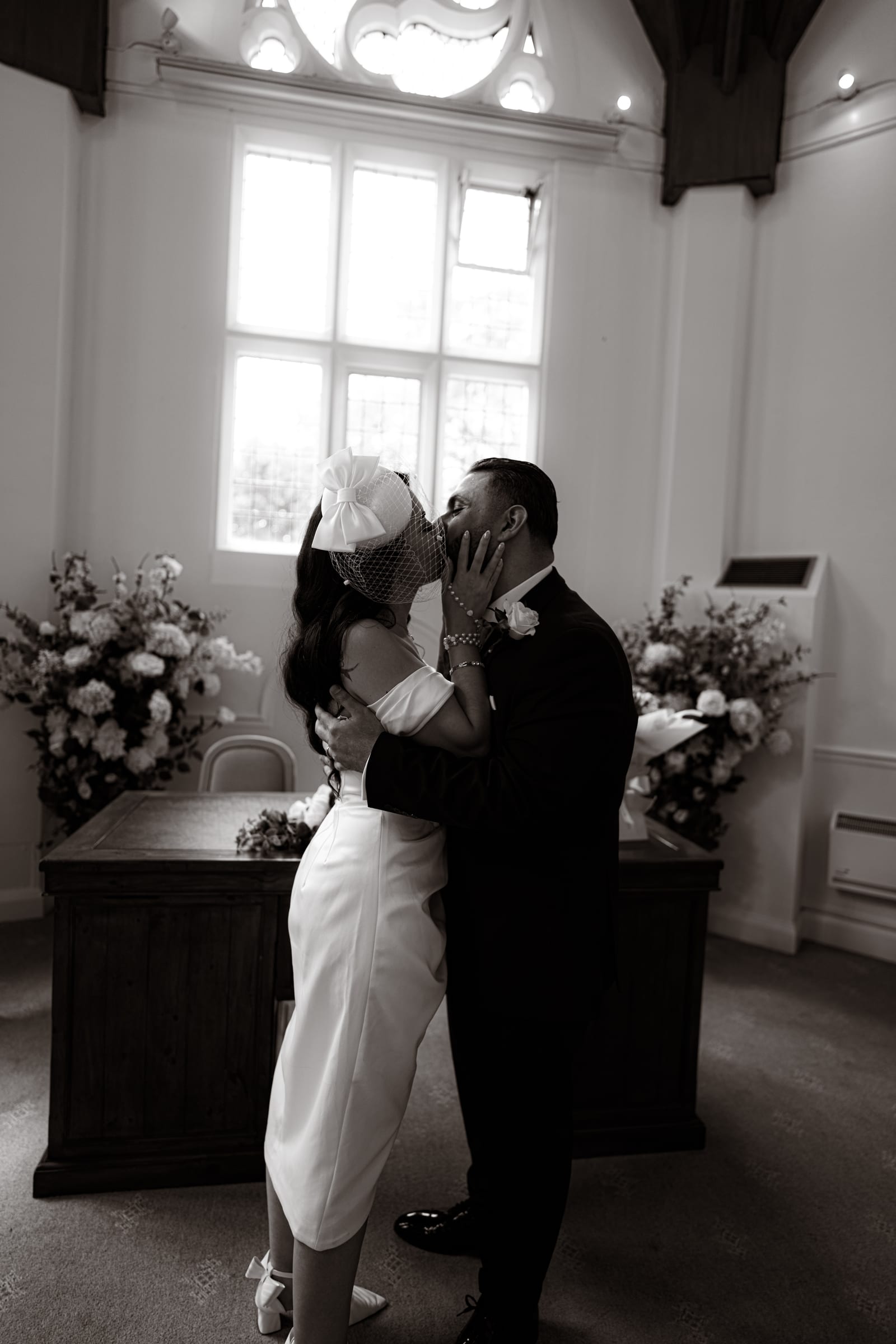 A first kiss beside the registrar’s desk under the vaulted ceiling at Cheshunt Register Office, in black and white