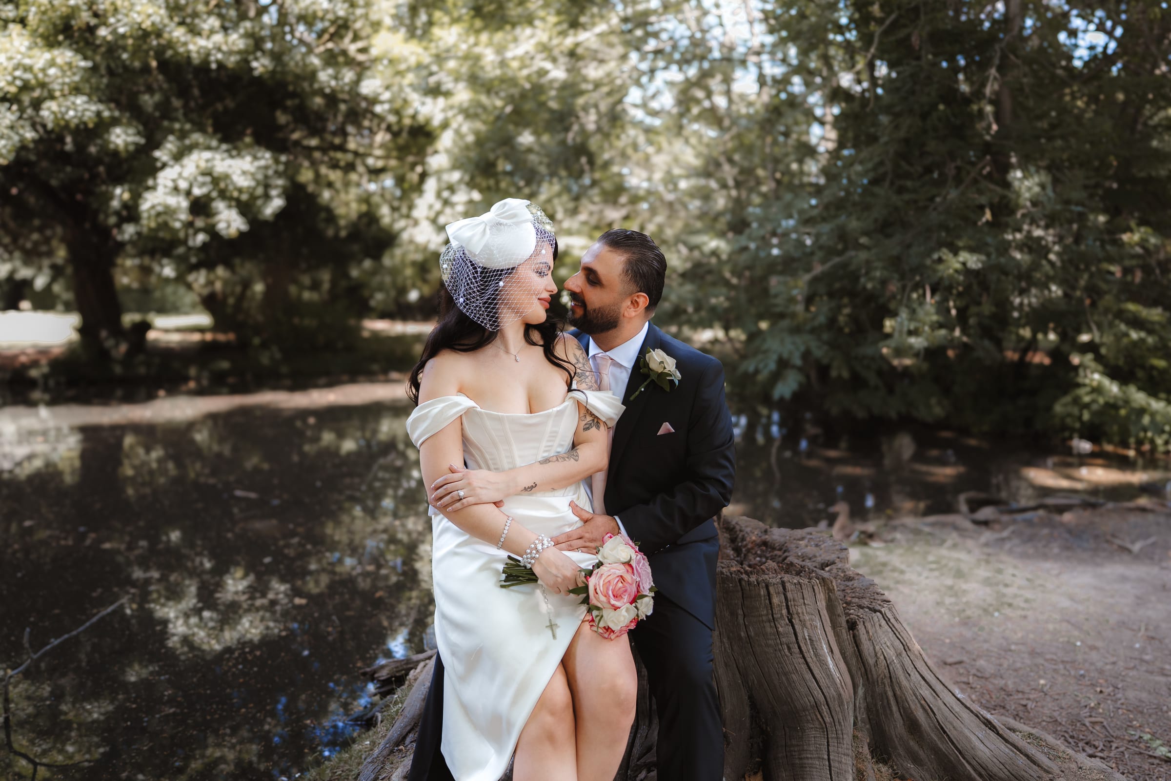 A newly married couple sitting on a fallen tree beside the lake in the gardens of Cheshunt Register Office