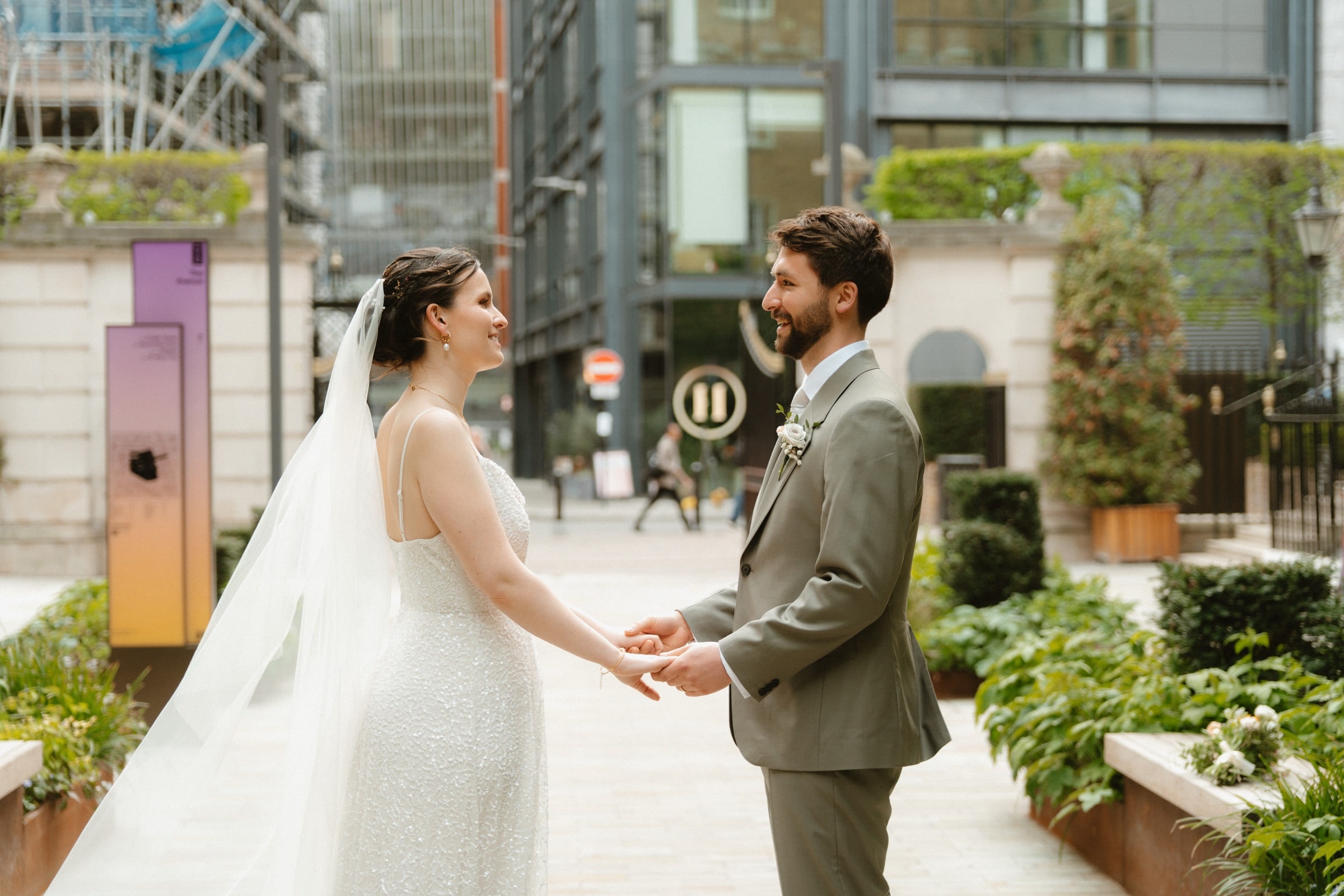 Bride and groom holding hands in a City of London courtyard, glass towers and greenery behind