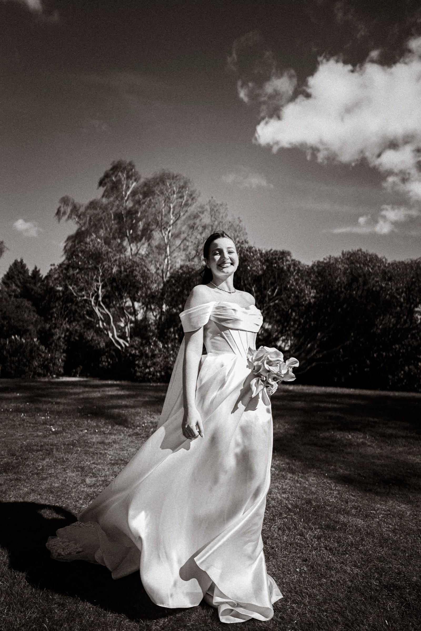 Black and white portrait of a laughing bride twirling her gown in the grounds of Highley Manor