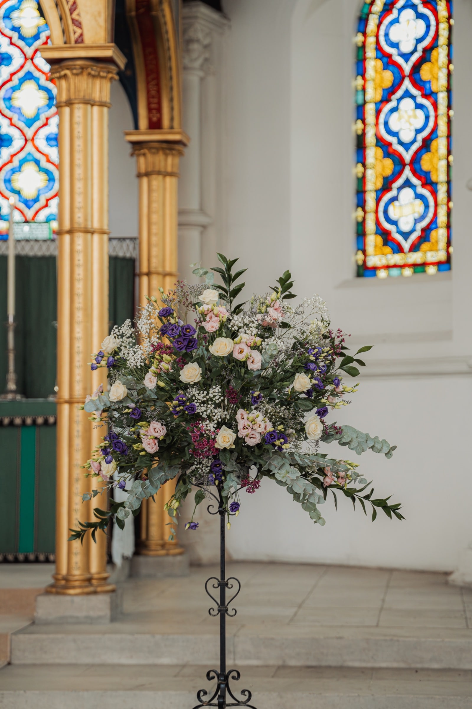 A wedding flower arrangement beside the gilded columns and vivid stained glass inside St John’s Church, East Dulwich
