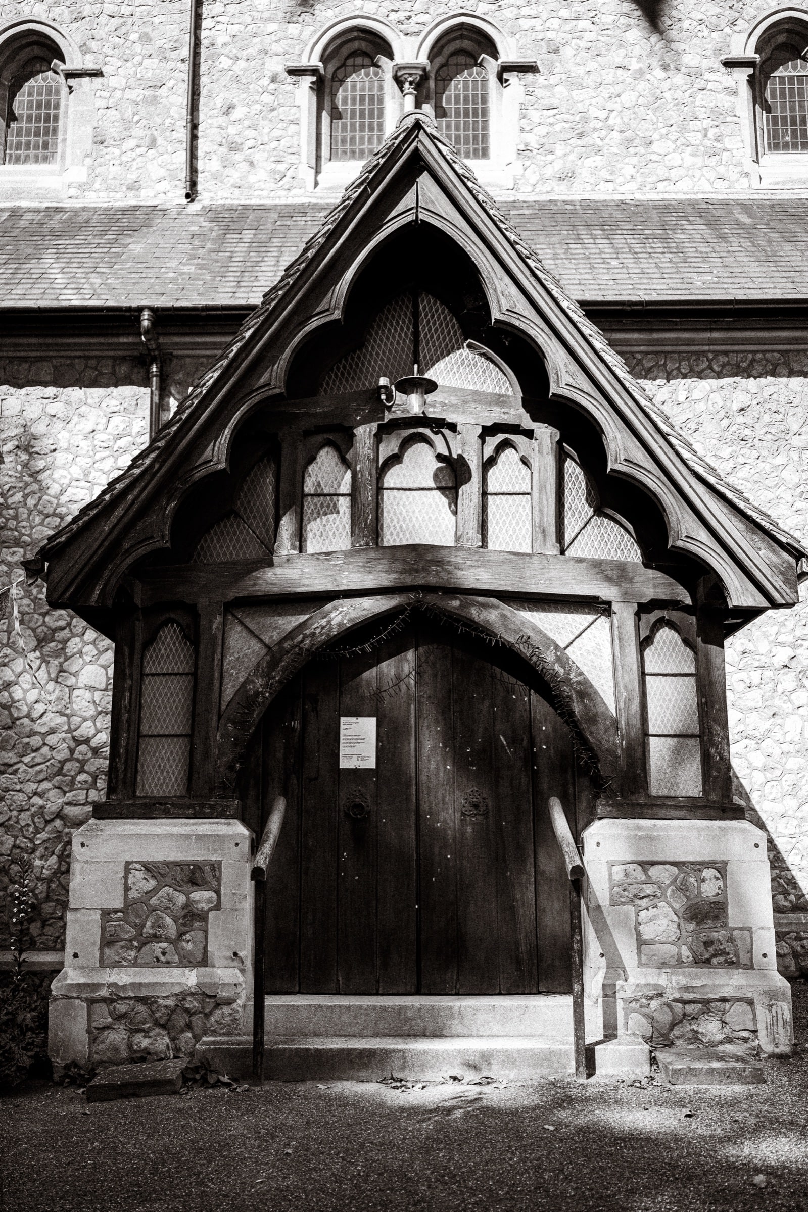The timber Gothic porch and arched oak door of St John’s Church, East Dulwich, in black and white