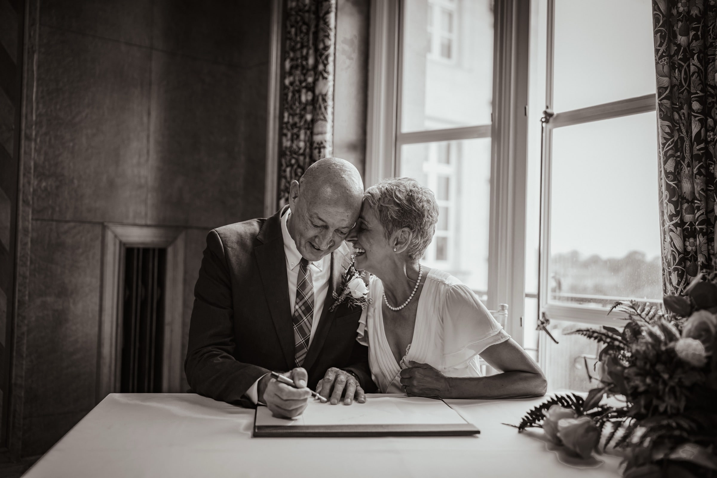 A couple laughing forehead to forehead as they sign the register at a London register office
