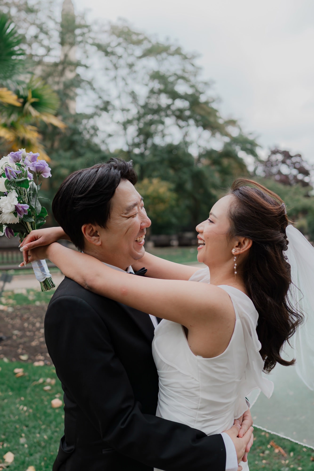 A couple laughing together in a leafy London park after their wedding