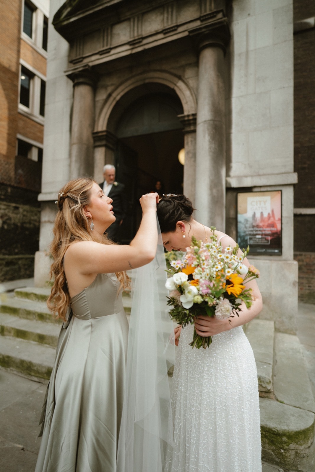 Bride having her veil adjusted outside All Hallows-on-the-Wall church, City of London