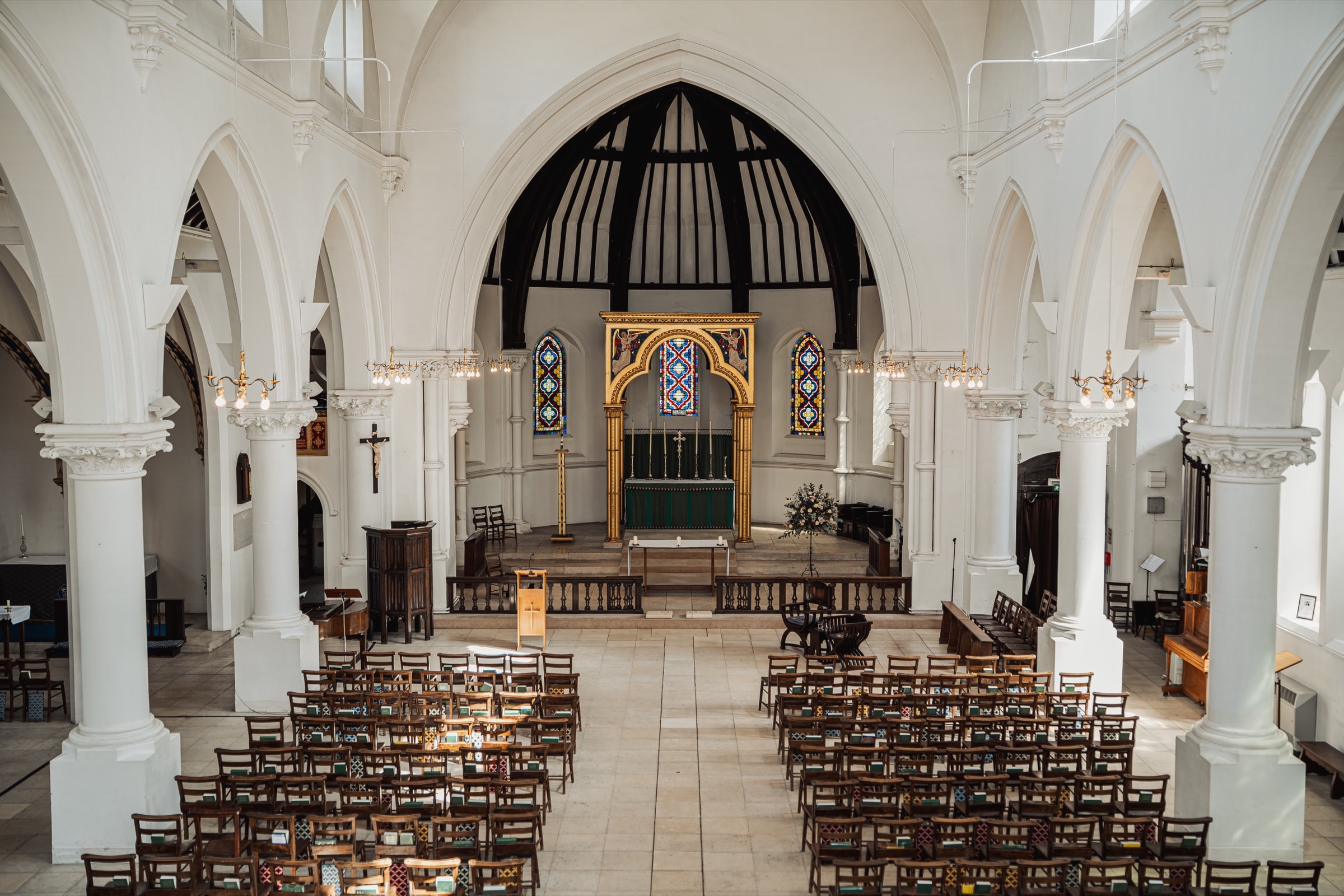 The white Gothic nave, gilded reredos and stained glass of St John’s Church, East Dulwich, set for a wedding ceremony