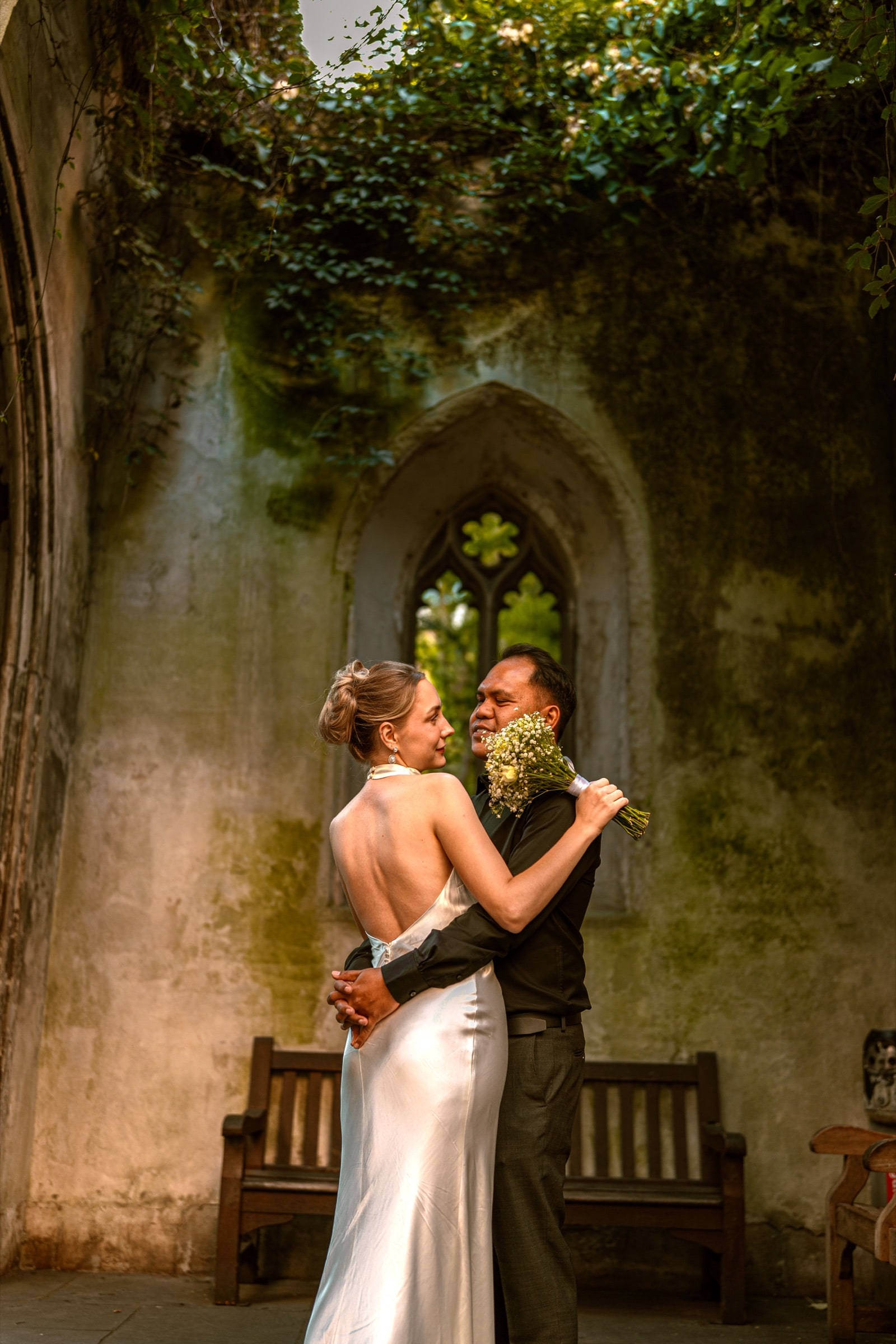 A couple embracing before the empty tracery window of St Dunstan in the East, ivy growing over the ruined walls