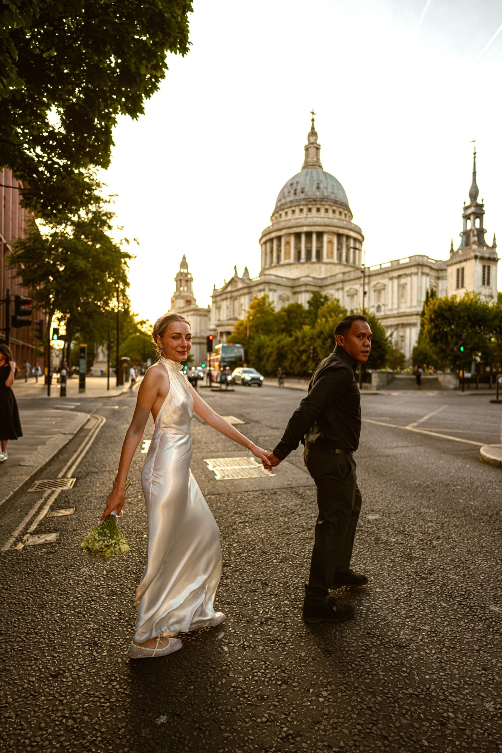A couple crossing the road hand in hand at golden hour, the dome of St Paul’s Cathedral filling the street behind them