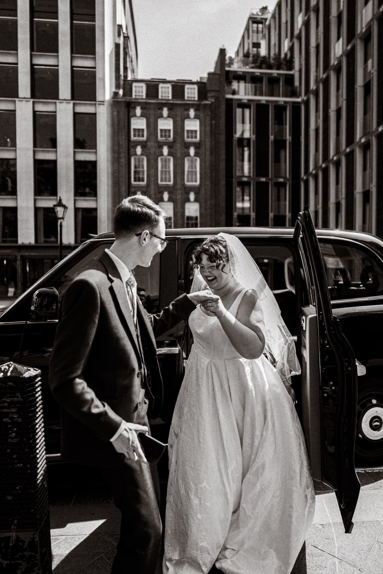 Black and white photograph of the bride stepping from a classic black London cab in the West End