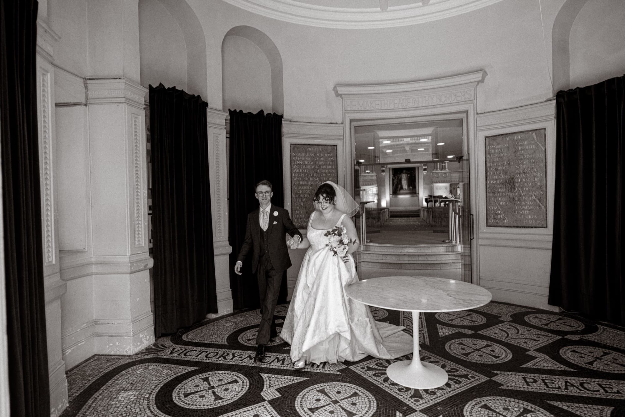 Black and white photograph of the bride arriving with her father across the mosaic floor at All Souls, Langham Place