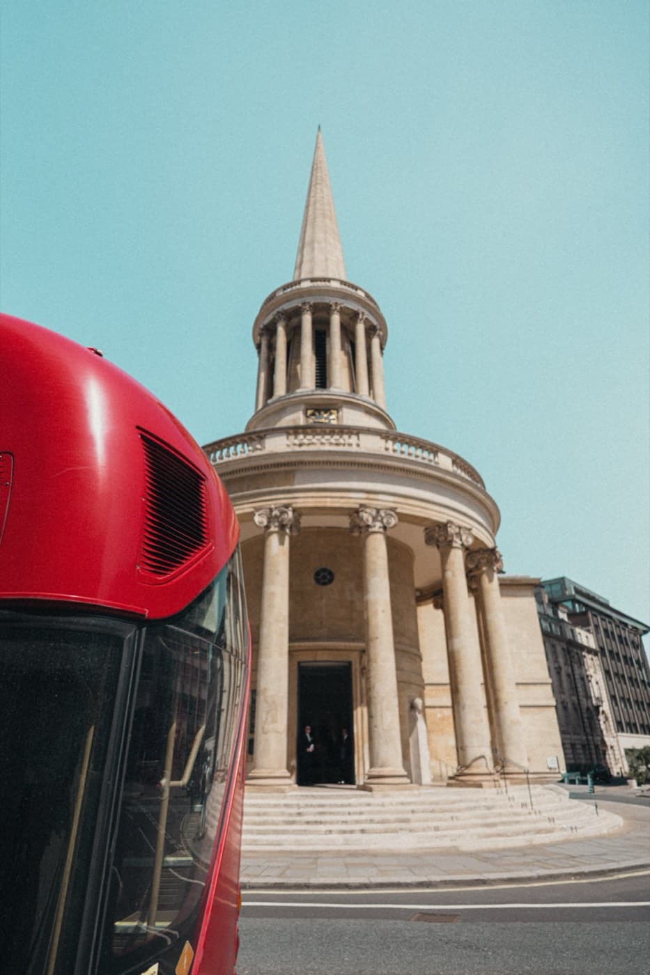 A red London bus passing the spire of All Souls, Langham Place, in central London