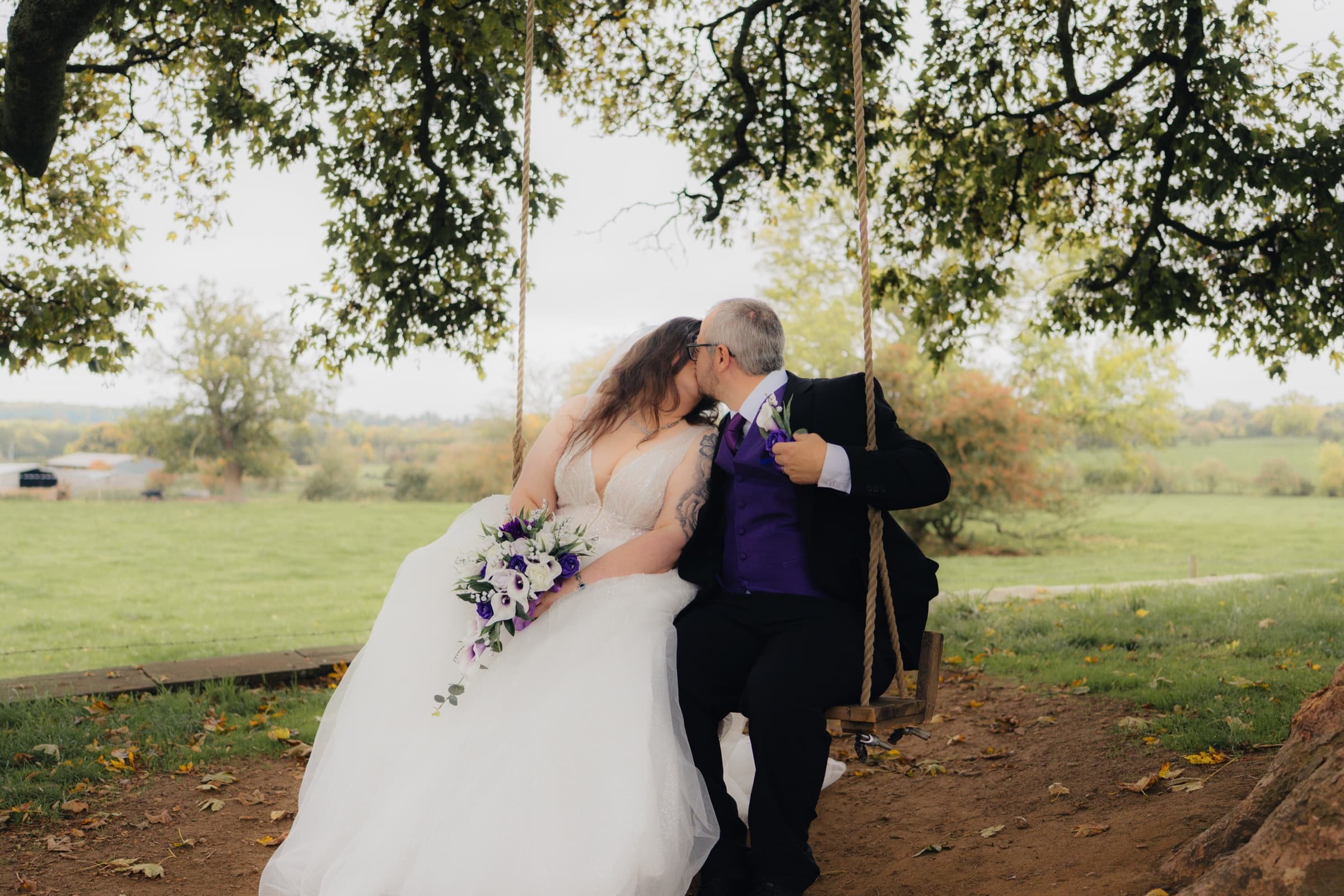Bride and groom kissing on a rope tree swing with open countryside behind at Ashton Lodge Country House