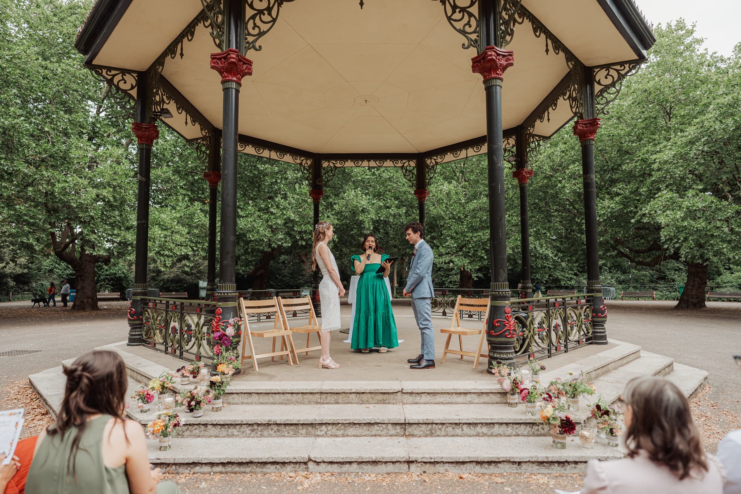 Outdoor wedding ceremony at the ornate Victorian bandstand in Battersea Park, London, framed by green trees