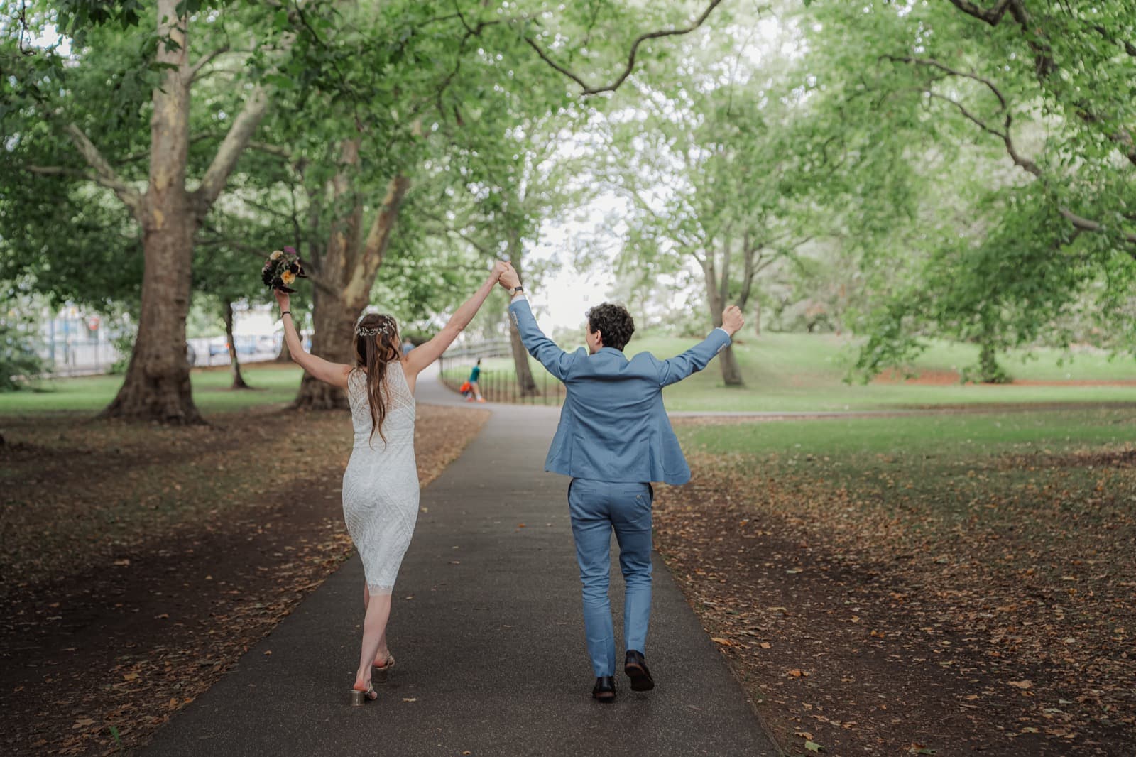 Couple walking hand in hand down a tree-lined avenue in Battersea Park