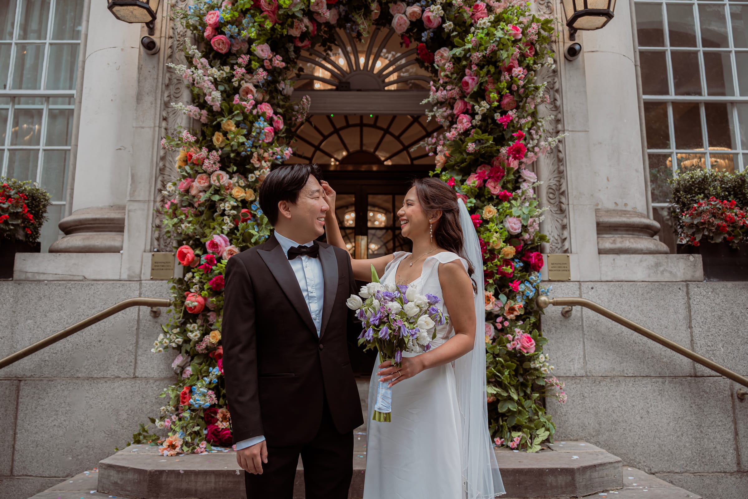 Newlyweds on the front steps of Chelsea Old Town Hall beneath the floral-arched King’s Road entrance
